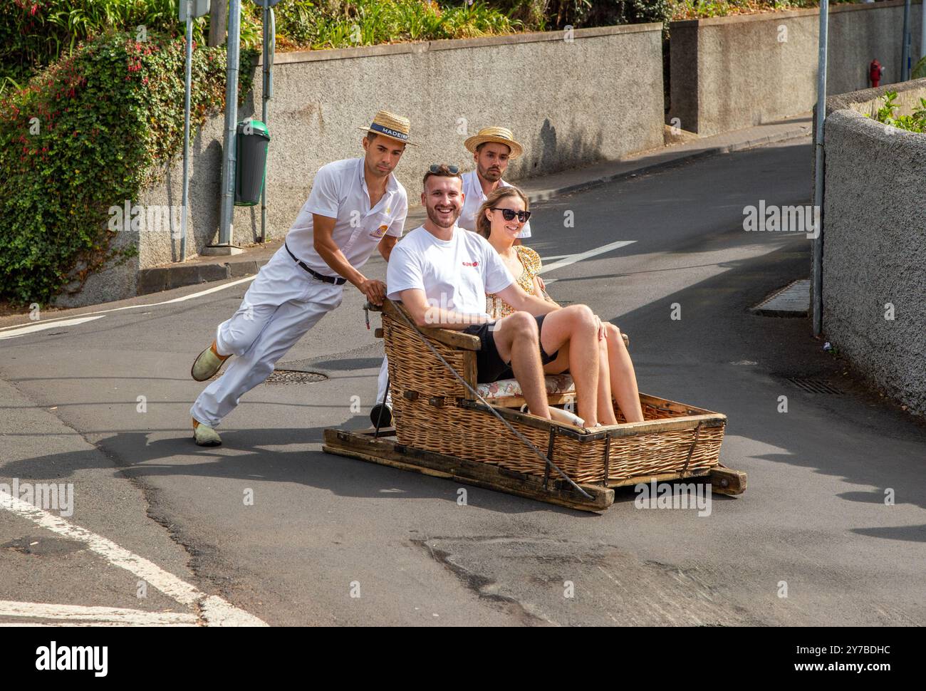 Urlauber und Touristen, die Spaß bei einer Fahrt mit traditionellen Korbrodelbahnen in Monte, Funchal auf der portugiesischen Insel Madeira haben Stockfoto