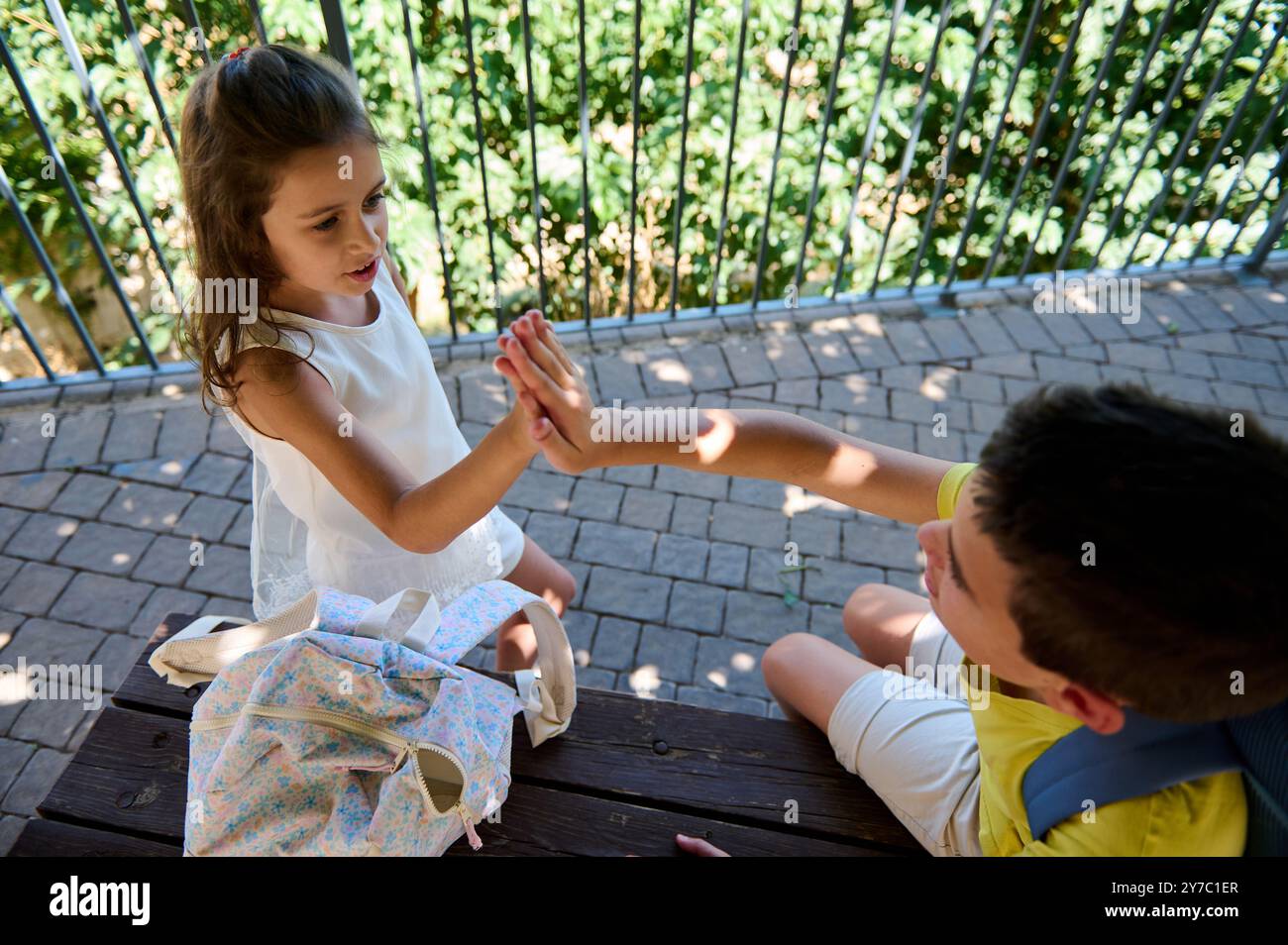 Zwei Kinder teilen sich an einem sonnigen Tag eine fröhliche High Five, die Freundschaft und Glück veranschaulicht. Rucksäcke empfehlen Schule oder Abenteuer. Stockfoto