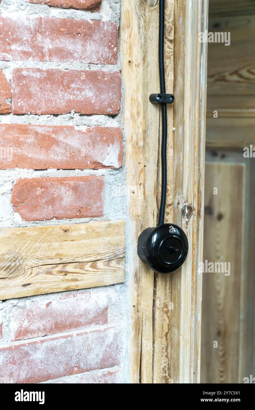 Klassischer elektrischer Schalter, Lichttaster mit schwarzem Elektrokabel, montiert an einer Fachwerkwand oder Fachwerkwand. Stockfoto