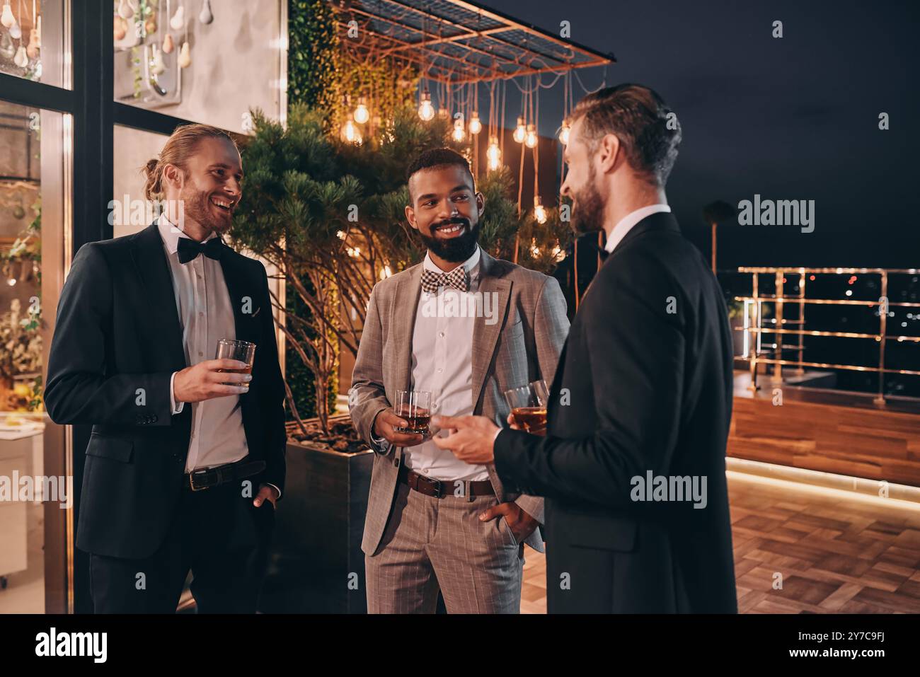 Drei gut gekleidete Männer trinken Whiskey und kommunizieren, während sie Zeit auf der Party verbringen Stockfoto