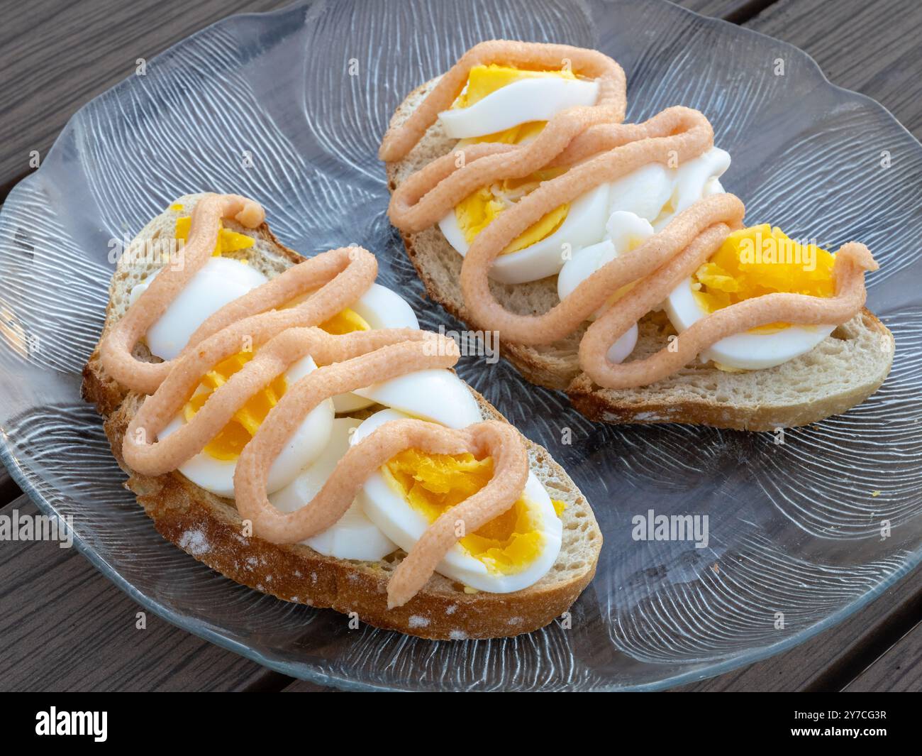 Zwei wunderschön gefertigte Sandwiches mit Eierscheiben und Kaviar im schwedischen Stil ruhen auf einer Glasplatte, die in einer Seitenansicht aufgenommen wird, um die Schichten von hervorzuheben Stockfoto