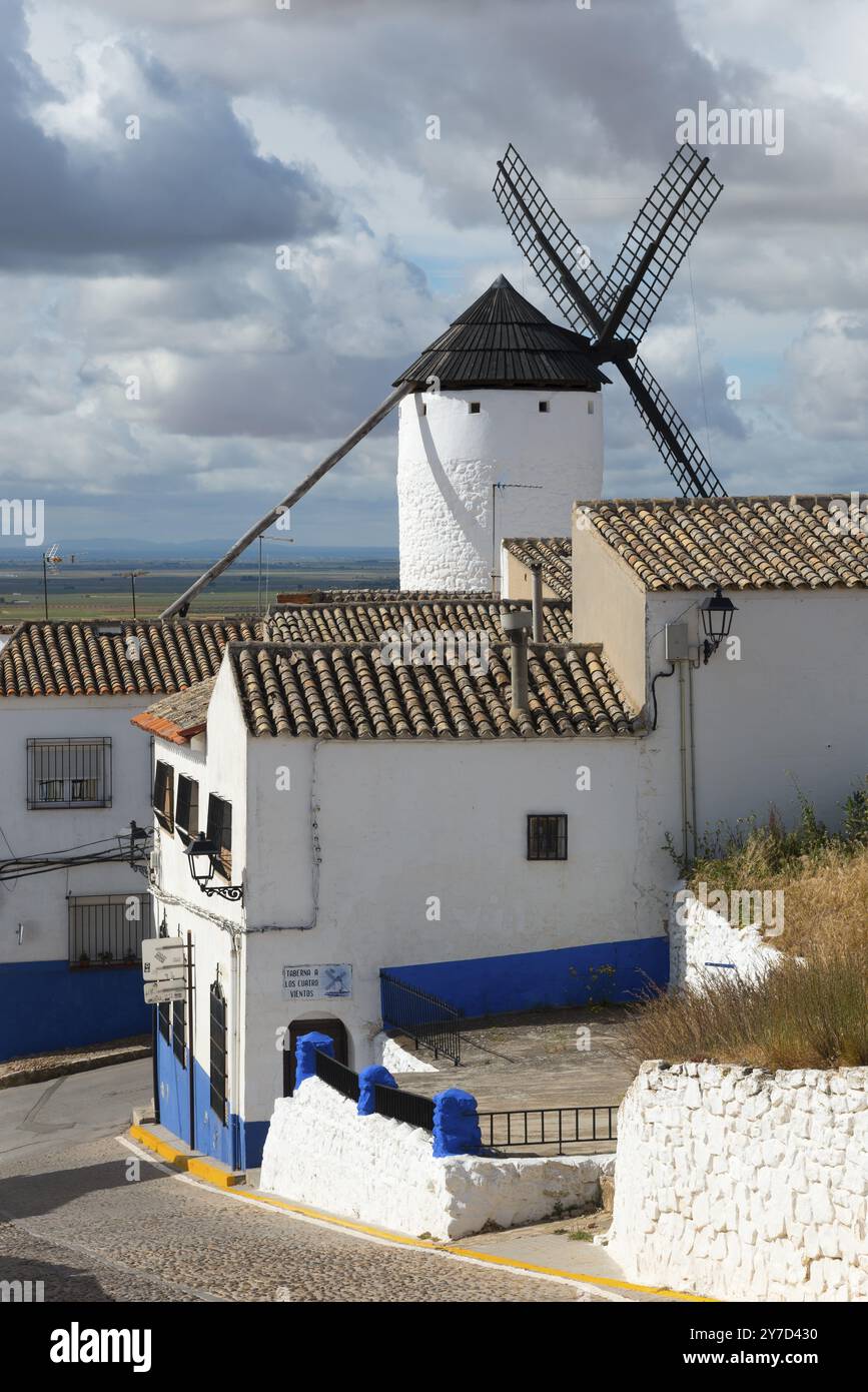 Weiße und blaue Häuser und Windmühle unter bewölktem Himmel in einem rustikalen Dorf, Campo de Criptana, Provinz Ciudad Real, Castilla-La Mancha, Route of Don Q Stockfoto