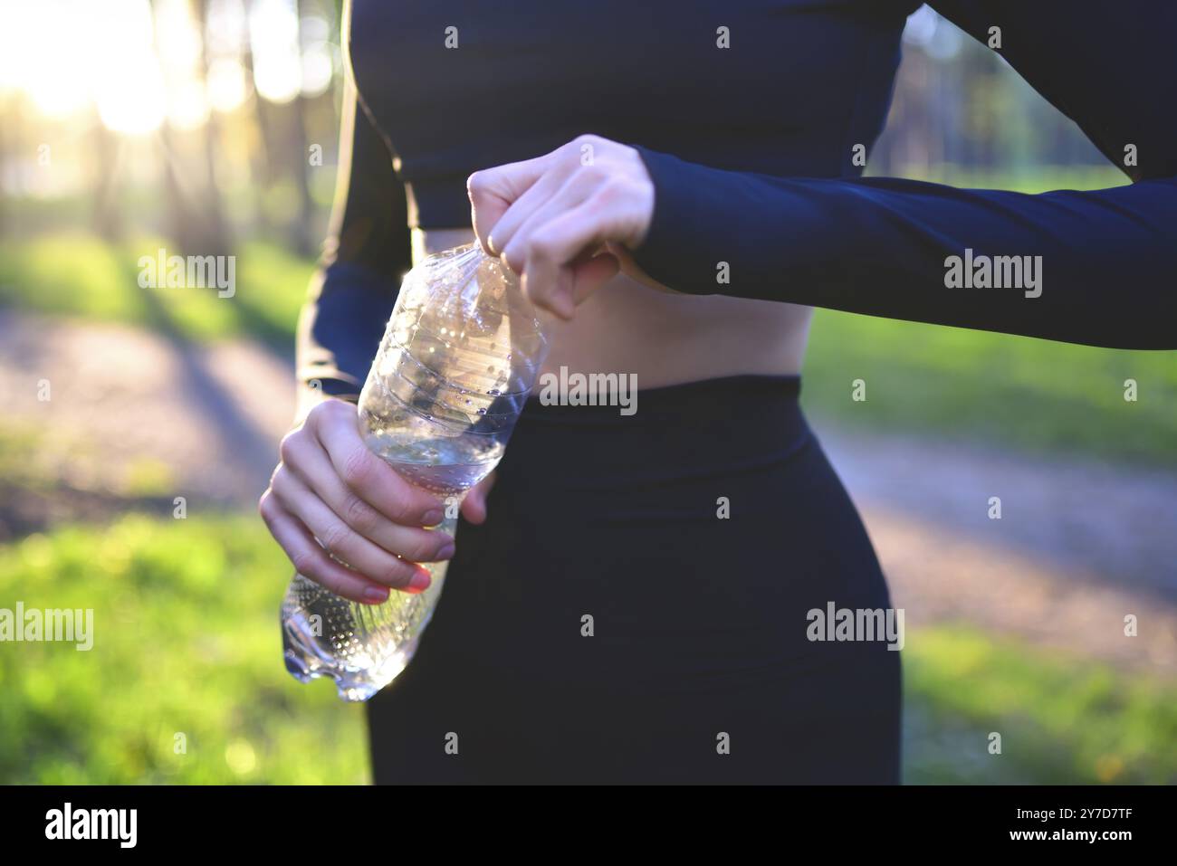 Frau in schwarzer Sportbekleidung, die eine Plastikflasche hält. Hydration während eines Workouts im Freien. Hidration Stockfoto