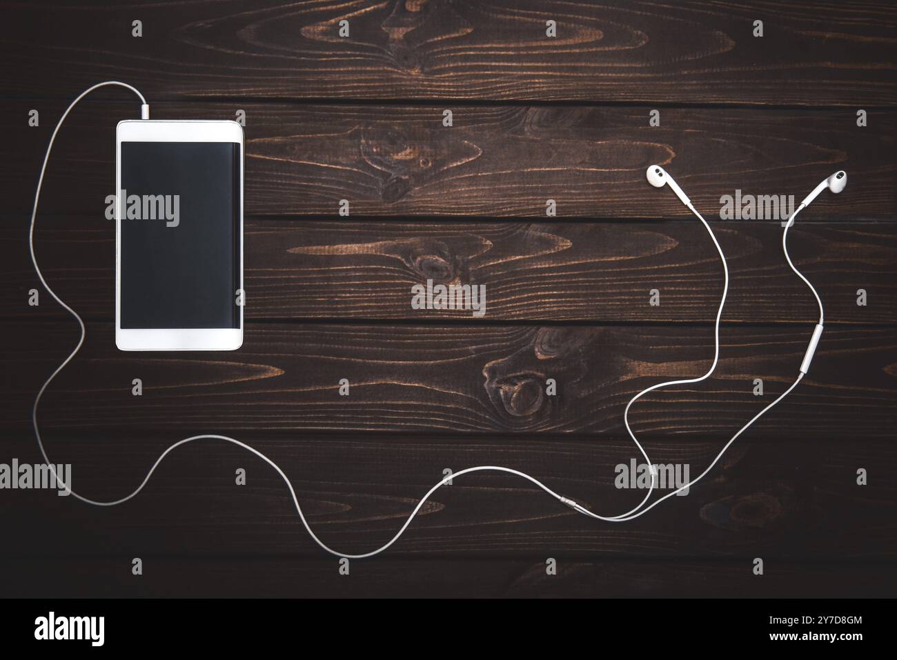 Weißes Smartphone mit weißen Kopfhörern auf hölzernem Hintergrund – Bild. Musik hören Stockfoto