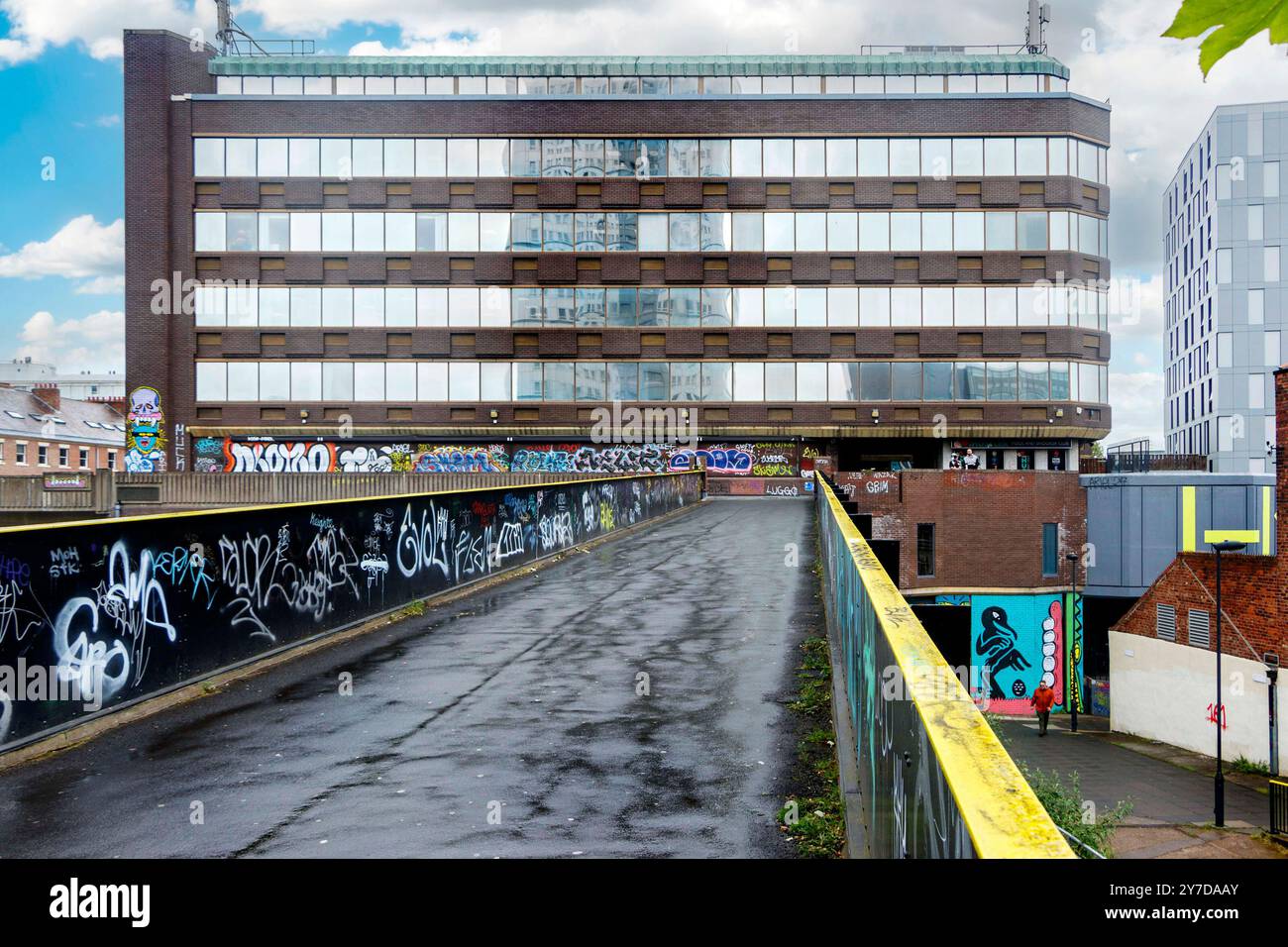 Eine urbane Szene mit einem großen Bürogebäude mit Graffiti-bedeckten Wänden und einem leeren, nassen Pfad, der zu ihm führt Stockfoto