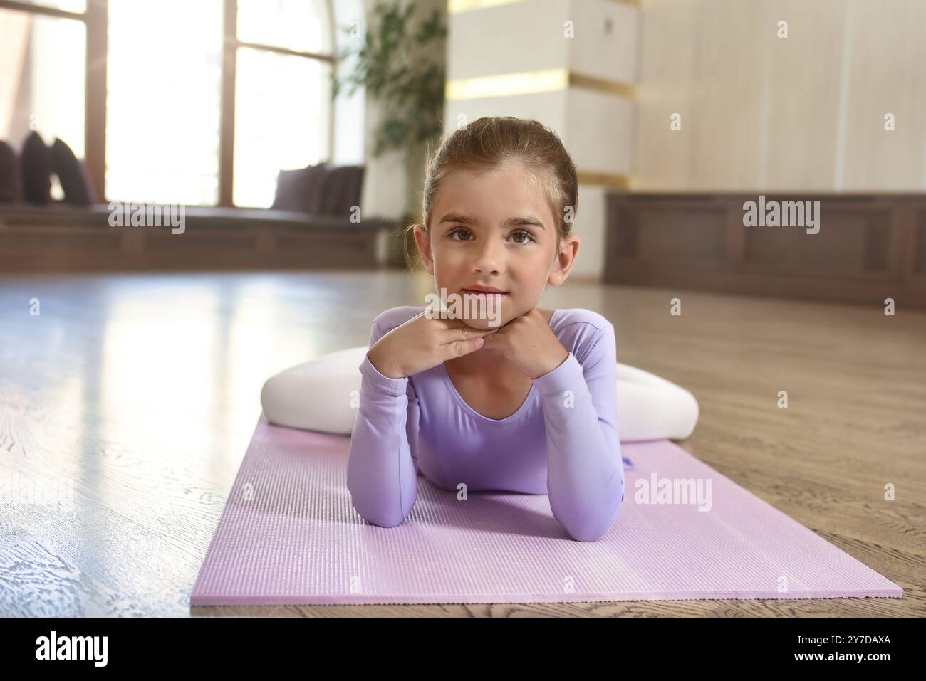 Ein kleines Mädchen in einem violetten Kleid, ein süßes lächelndes Mädchen, das auf einer Sportmatte liegt Stockfoto