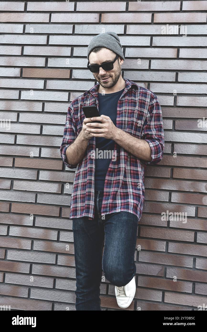 Hipster sms Phone App in Stadt Straße Mauer Hintergrund. Erstaunlicher Mann holding Smartphone in Smart Casual Wear stehen. Urban young profe Stockfoto