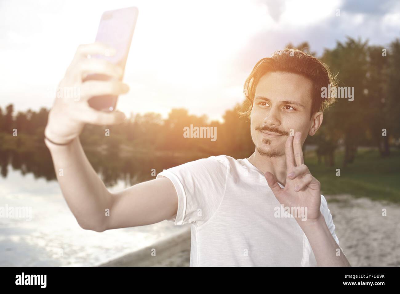 Porträt des jungen, hübschen, lächelnden Mannes, der Selfie gegen den See macht. Wunderschöne Natur Stockfoto