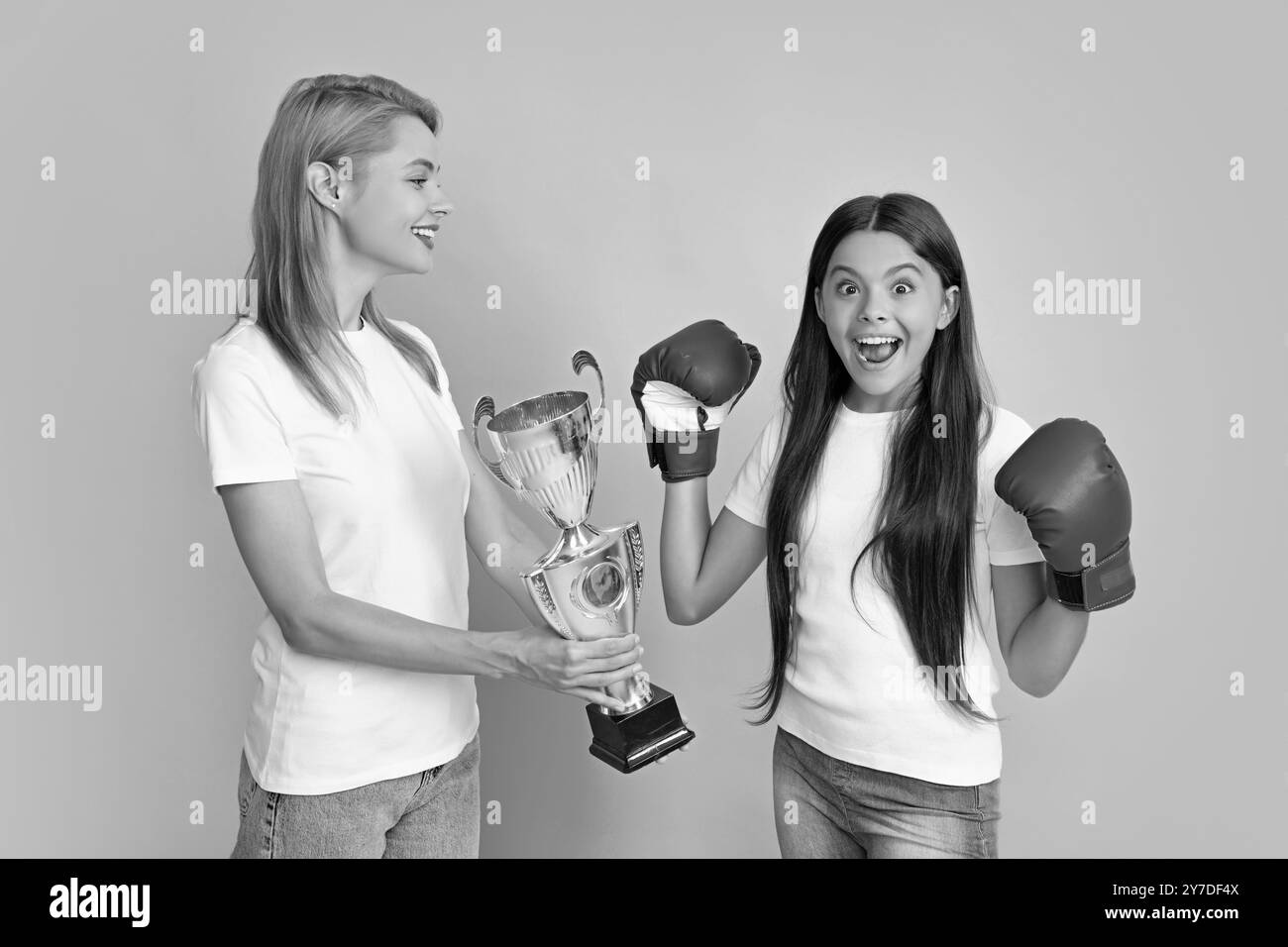 Mama und Tochter eines Teenagers halten den Siegerpreis und zeigen die Trophäe vor blauem Hintergrund. Eltern unterstützen Mädchen Kind, den Sieg zu feiern Stockfoto