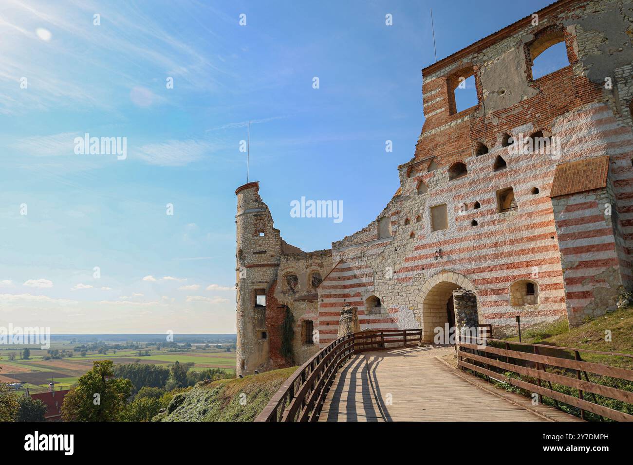 Mittelalterliche Burgruinen mit gestreiften Steinmauern und einem Holzsteg. Das Gebäude überblickt eine ländliche Landschaft unter einem hellblauen Himmel, Showcasin Stockfoto