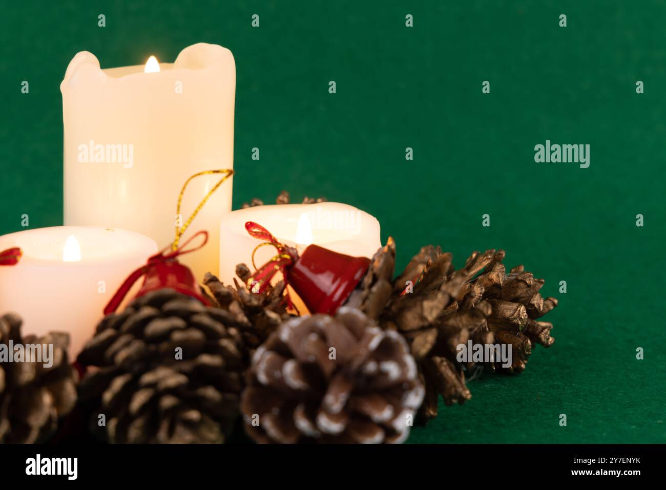 Wunderschön gestaltetes Weihnachtszentrum mit leuchtenden Kerzen und Tannenzapfen mit roten Glocken vor grünem Hintergrund Stockfoto