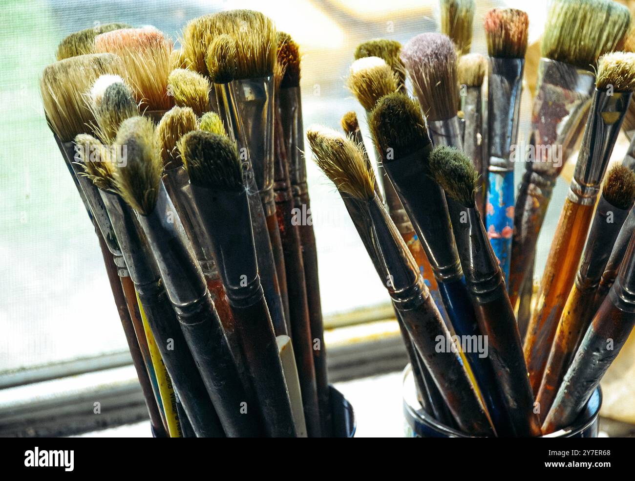Fotografie von zwei Gläsern mit gut gebrauchten Künstlerpinseln auf der Fensterbank Stockfoto