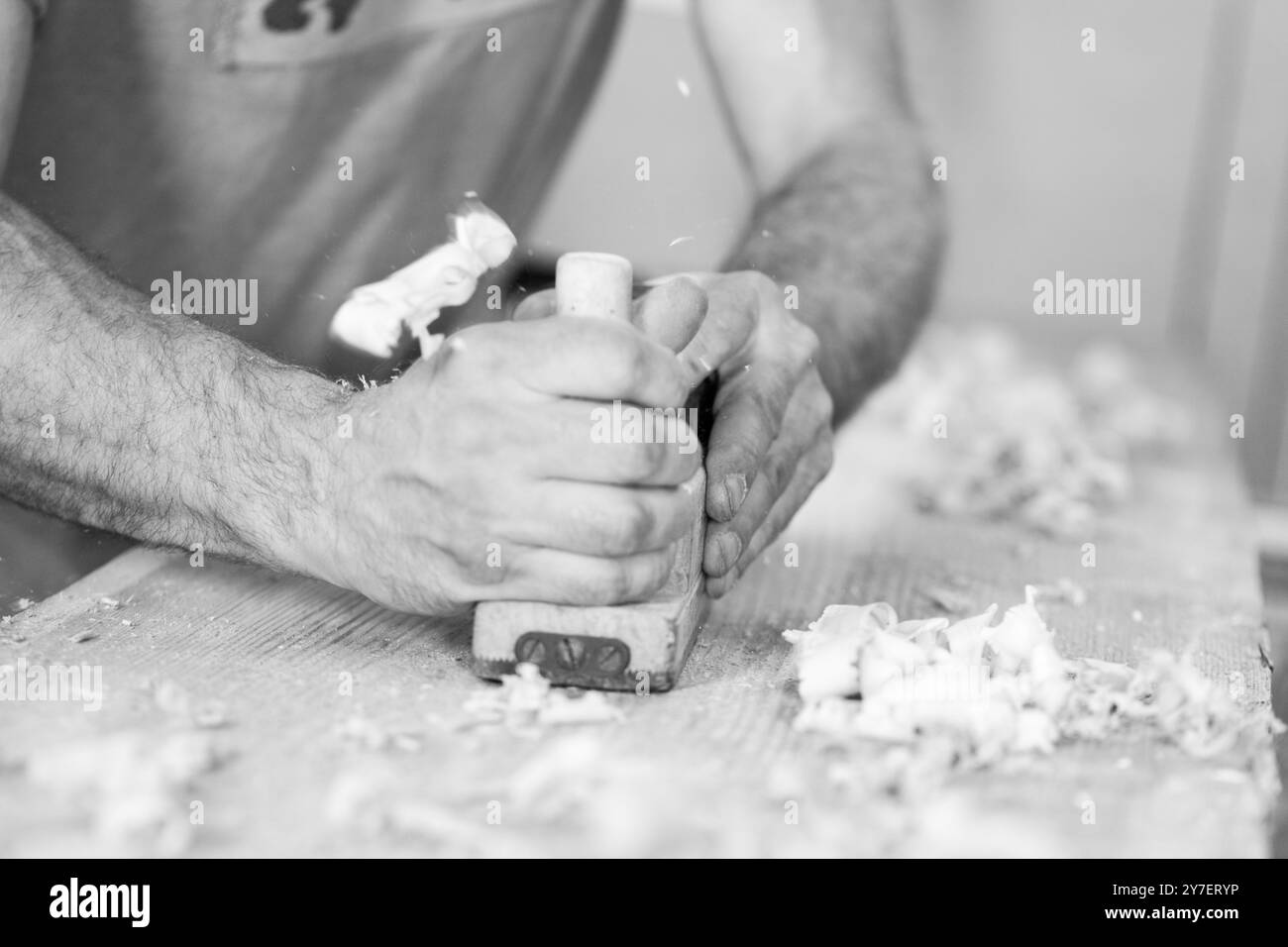 Der Zimmermann formt ein Stück Holz sorgfältig mit einem Handflugzeug, seine Hände mit Sägemehl bedeckt. - Schwarz n weiß - Stockfoto