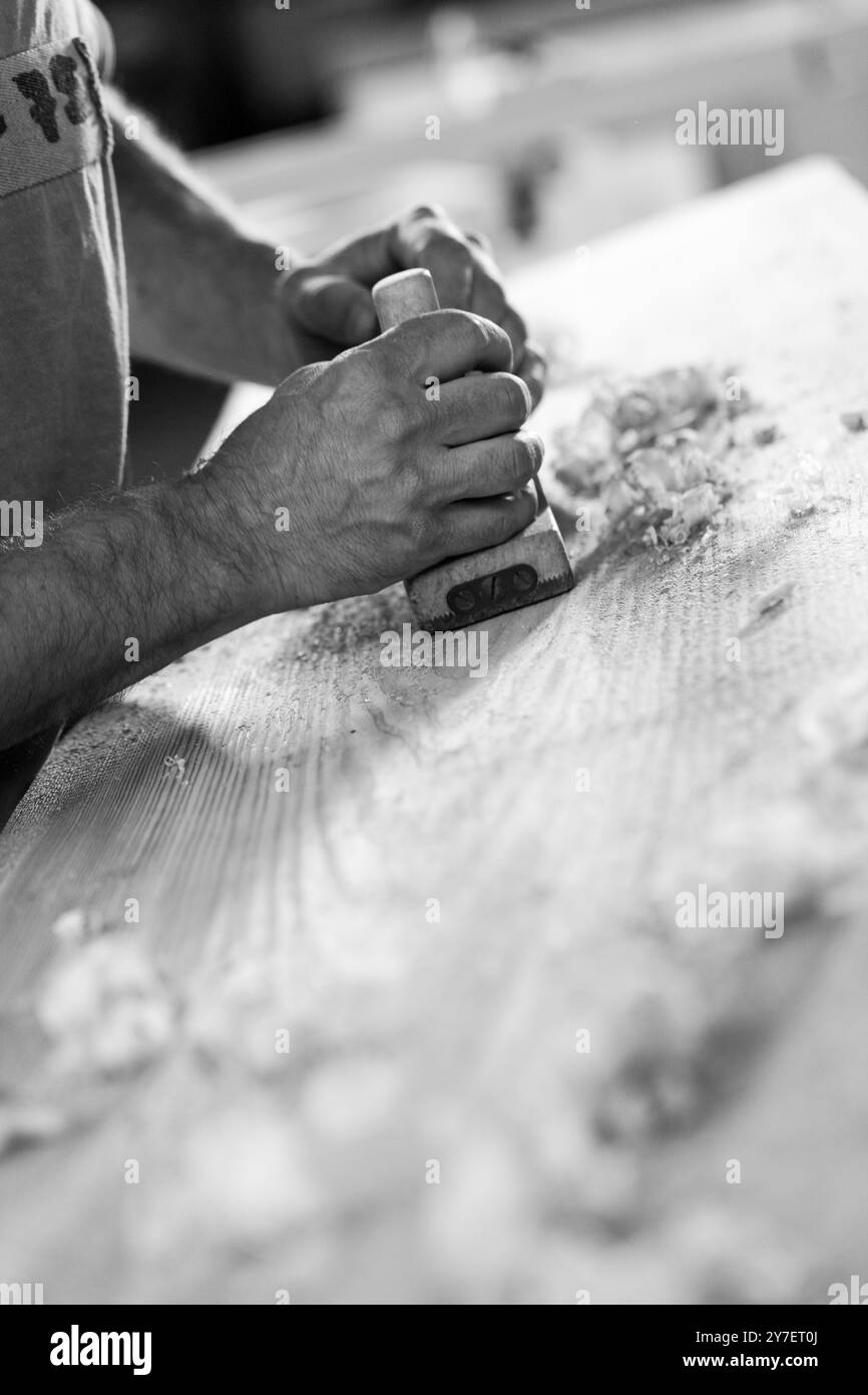 Nahaufnahme der Zimmermannshände, die eine Holzdiele mit einem Schleifblock glätten, mit Sägemehl im Vordergrund. - Schwarz n weiß - Stockfoto