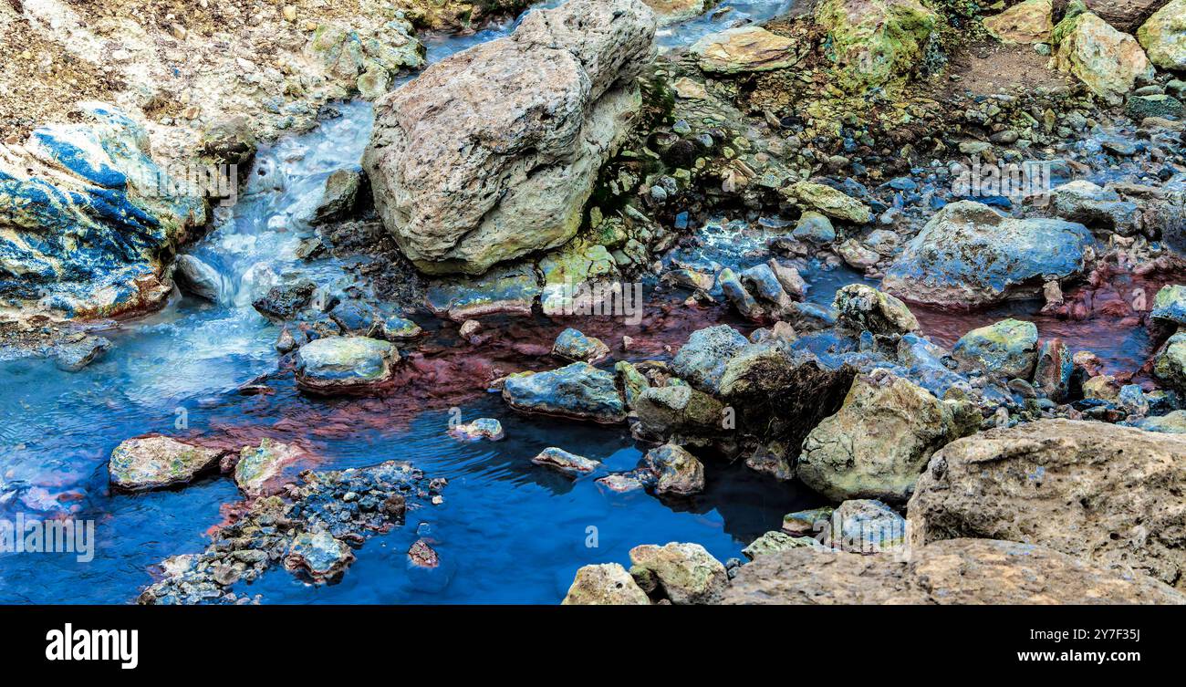 Ein Wasserstrom fließt durch ein felsiges Gebiet. Das Wasser ist blau und die Felsen sind voller Farben Stockfoto