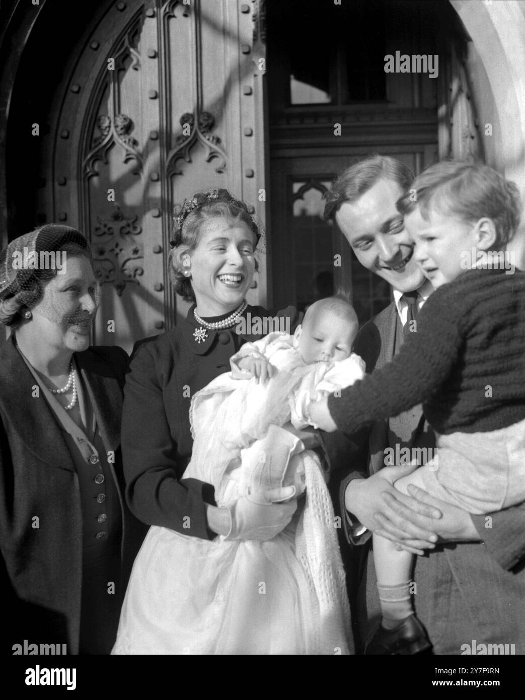 Der junge Hilary James liegt nach seiner Taufe in der Krypta des House of Commons glücklich in den Armen seiner Mutter. Er ist der zweite Sohn von Anthony Wedgewood Benn, der den älteren Sohn Stephen Michael, 2, hält. März 1954 Stockfoto