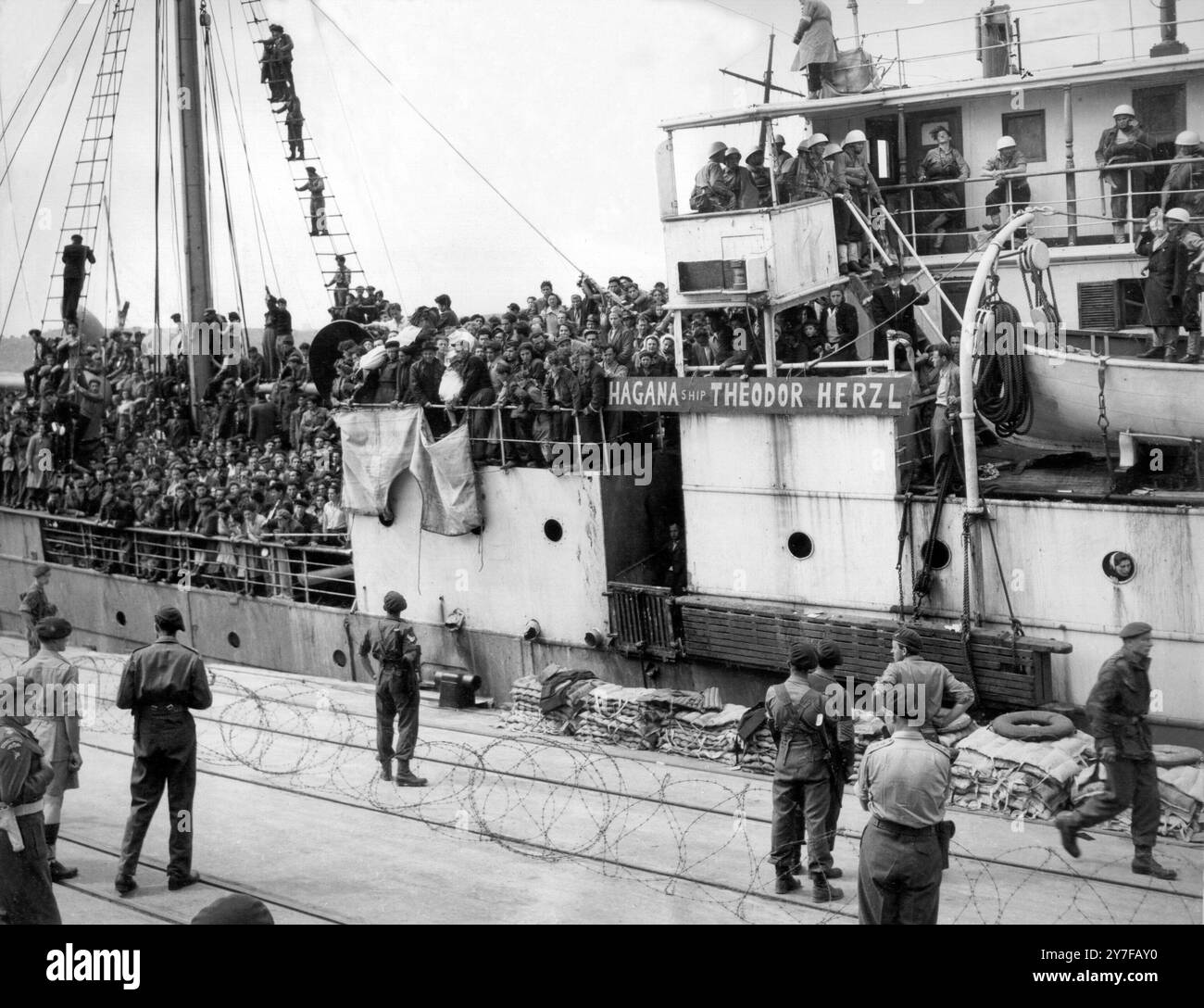Das Foto wurde im Hafen von Haifa aufgenommen, als 2700 illegale jüdische Einwanderer aus dem „Guardian“ ausstiegen, einem der größten illegalen Schiffe, die von Heck zu Heck überfüllt anliefen. An Deck lagen die Leichen von zwei Männern, die bei einem Zusammenstoß getötet wurden, in jüdische Fahnen gehüllt. Die Leichen hochgehalten, riefen die Einwanderer zu den Soldaten auf dem Steg: "Du hast sie getötet. Runter mit Bevins Regierung. Trotzdem verließen die Einwanderer das Schiff ohne Widerstand. Es waren 24 Babys an Bord. Foto zeigt: Die Leichen der beiden Toten werden aus Protest hochgehalten, während das Schiff am Kai liegt. April 1947 Stockfoto
