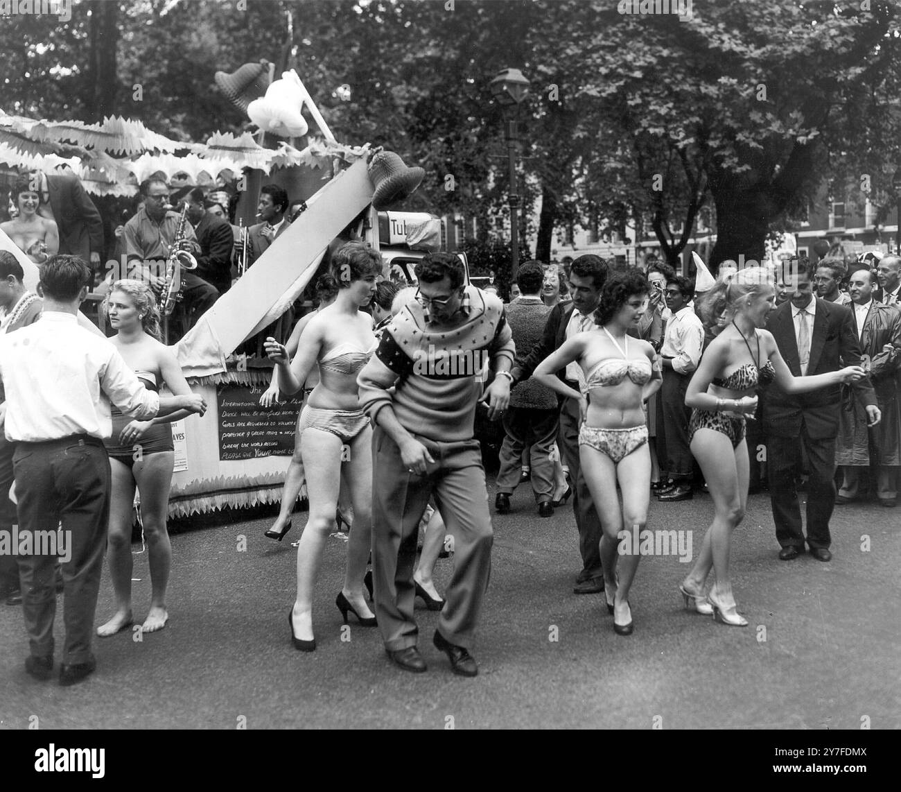 Akzent auf der Rolle. London: Mit viel Akzent auf der Rolle während einer Show von Rock 'n Roll stehen diese Mädchen zu Beginn der Karnevalsprozession am Eröffnungstag der Soho Fair Week auf der Straße. Die Girls repräsentieren den Club de La Cote D'Azur, einen der vielen beliebten Nachtclubs in Soho, die an der Soho-Woche teilnehmen, um die Öffentlichkeit zu unterhalten und in den Bezirk zu locken. Juli 1957. Stockfoto