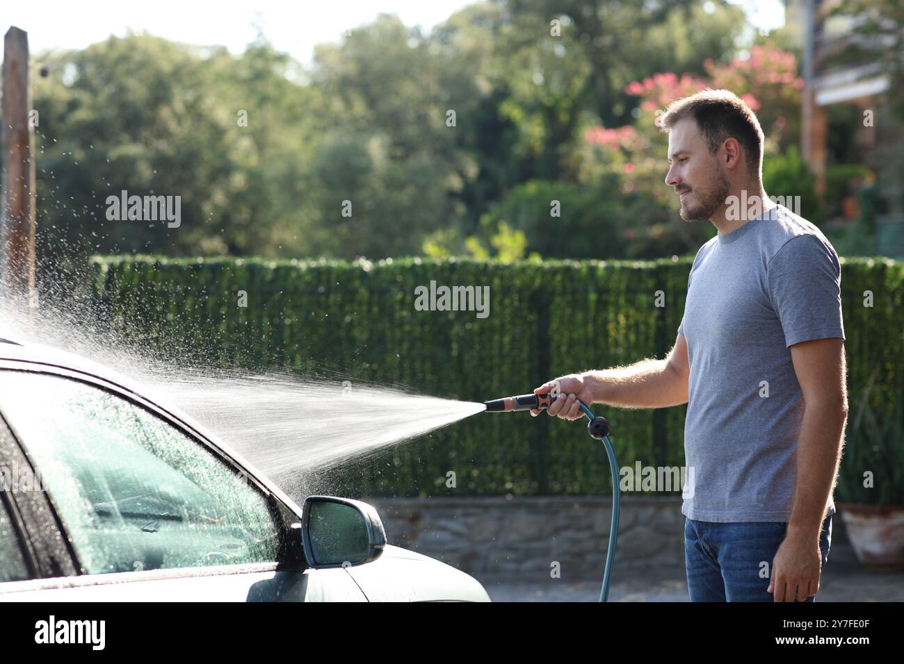 Mann, der das Auto mit Wasser reinigt, indem er im Garten einen Schlauch benutzt Stockfoto