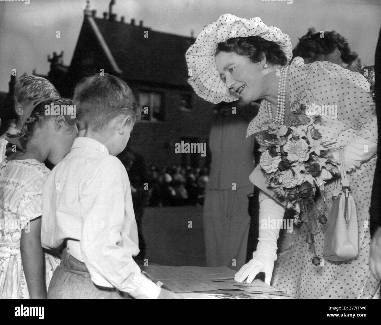 Königin Elizabeth, die Königin Mutter, in coolem Sommeroutfit, bummt sich, um ein Blumenmalbuch anzusehen, das ihr der siebenjährige Jeffrey Ward bei ihrem Besuch in Lond Gardens am 27. Juni 1957 gezeigt hat Stockfoto