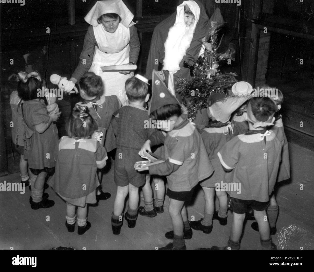 Kinder in einem Kindergarten für Kinder unter fünf Jahren, deren Väter hauptsächlich in der Armee sind und ihre Mütter arbeiten. Eine Krankenschwester überreicht Weihnachtsgeschenke an eifrige Kinder. Dezember 1940 Stockfoto