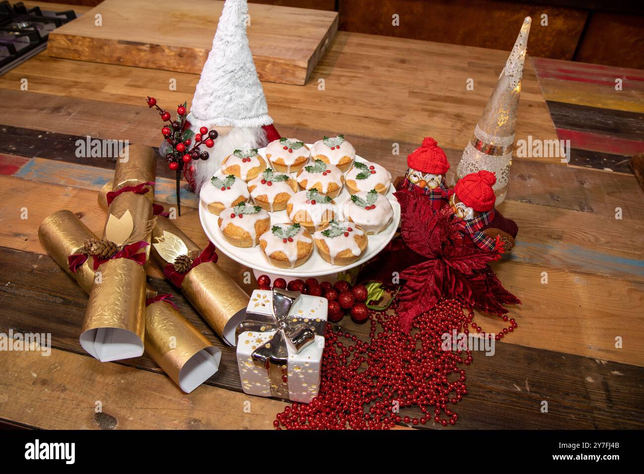 Ein Teller mit leckeren Weihnachts-Hackkuchen, bedeckt mit Glasur und essbarer stechpalme, umgeben von britischen Weihnachts-Crackern und festlichen Artikeln Stockfoto