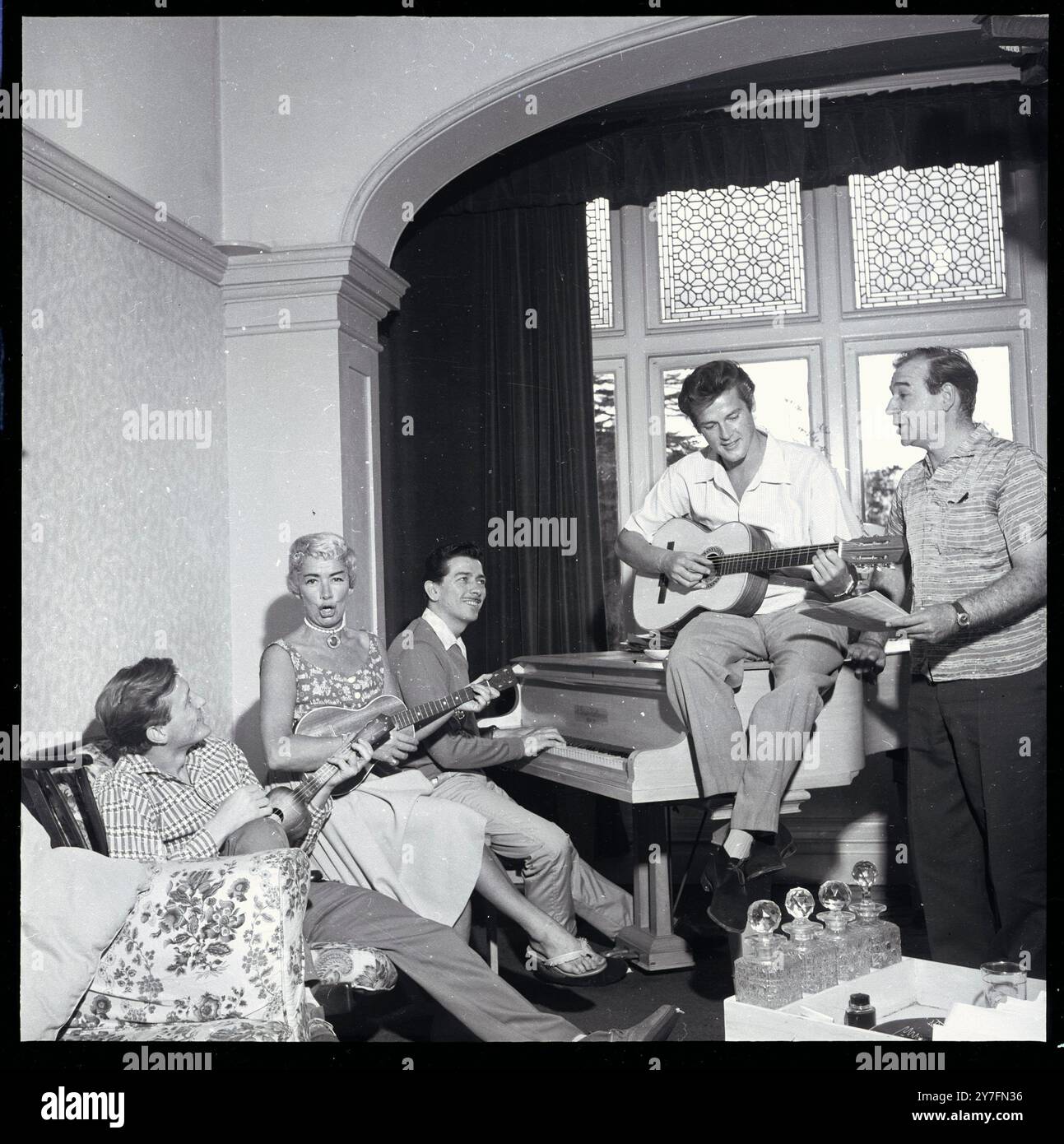 Roger Moore 1958. Im britischen Haus, das er mit seiner Frau Dorothy Squires teilte, The Mount, Wansunt Road, Bexleyheath. Piano-Spieler ist Tony Osborne, weit links Gary Miller (Sänger, großer Hit Robin Hood-Thema) ganz rechts Robert Brown, dann Squire Gurth in Ivanhoe mit Moore, später M in den James-Bond-Filmen von 1981. Stockfoto