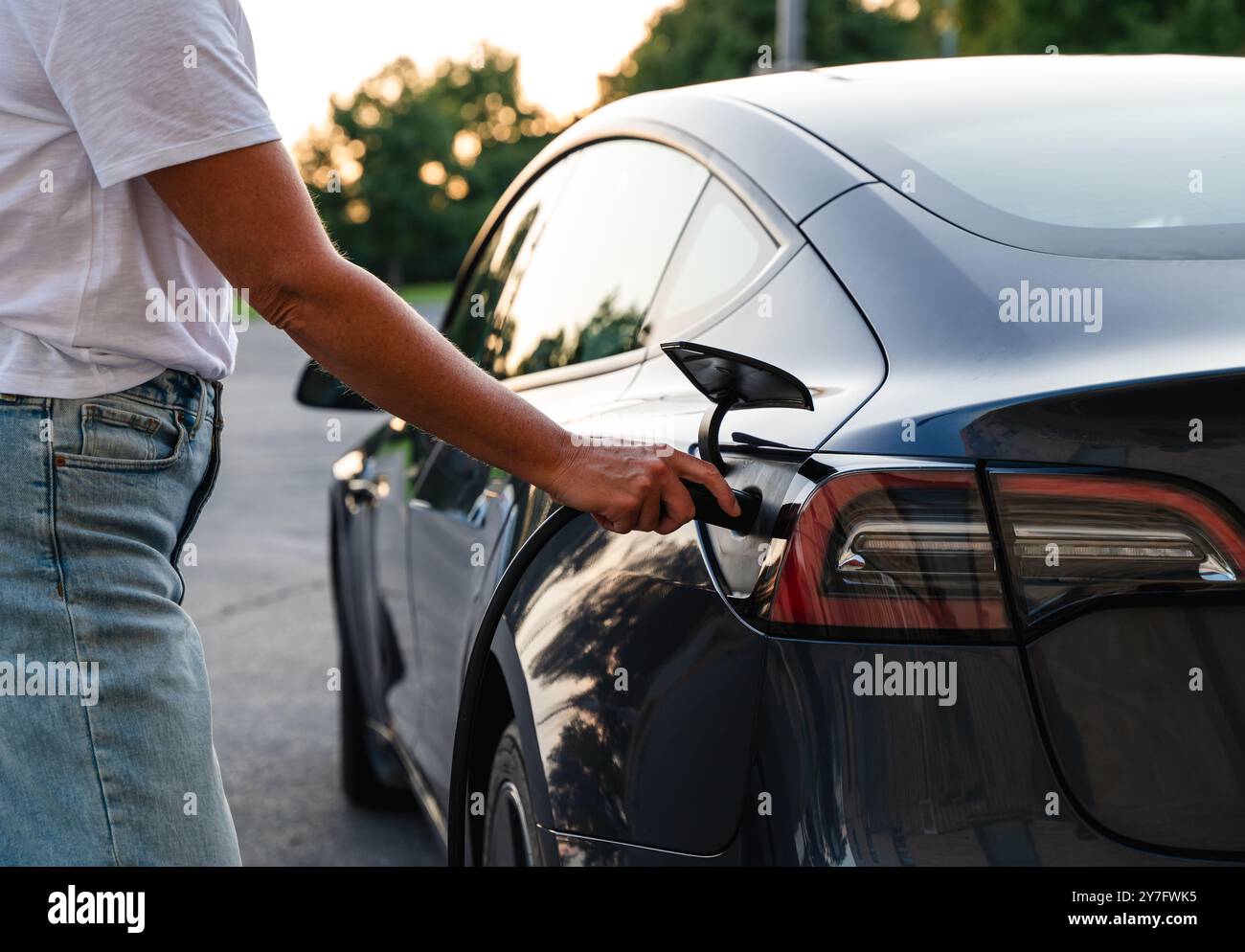 Nahaufnahme einer Frau, die draußen ein EV-Ladegerät an ein Elektrofahrzeug angeschlossen hat. Stockfoto