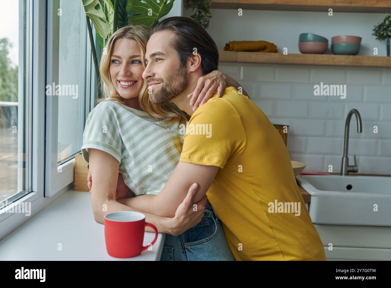 Wunderschönes junges Paar, das durch ein Fenster schaut, während er in der Küche steht Stockfoto