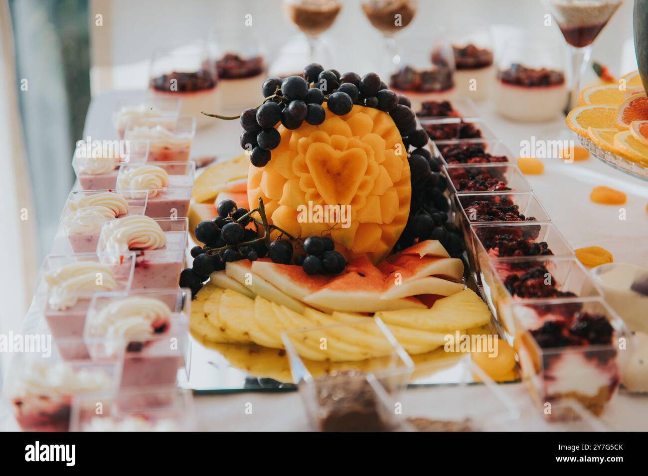 Ein wunderschön gestalteter Desserttisch mit geschnitztem Obst und verschiedenen Desserts in kleinen Tassen. Stockfoto