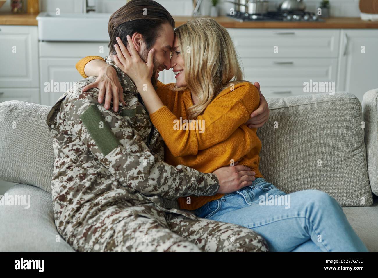 Junger Mann in militärischer Form, der seine Frau umarmt, nachdem er aus dem Krieg nach Hause gekommen ist Stockfoto