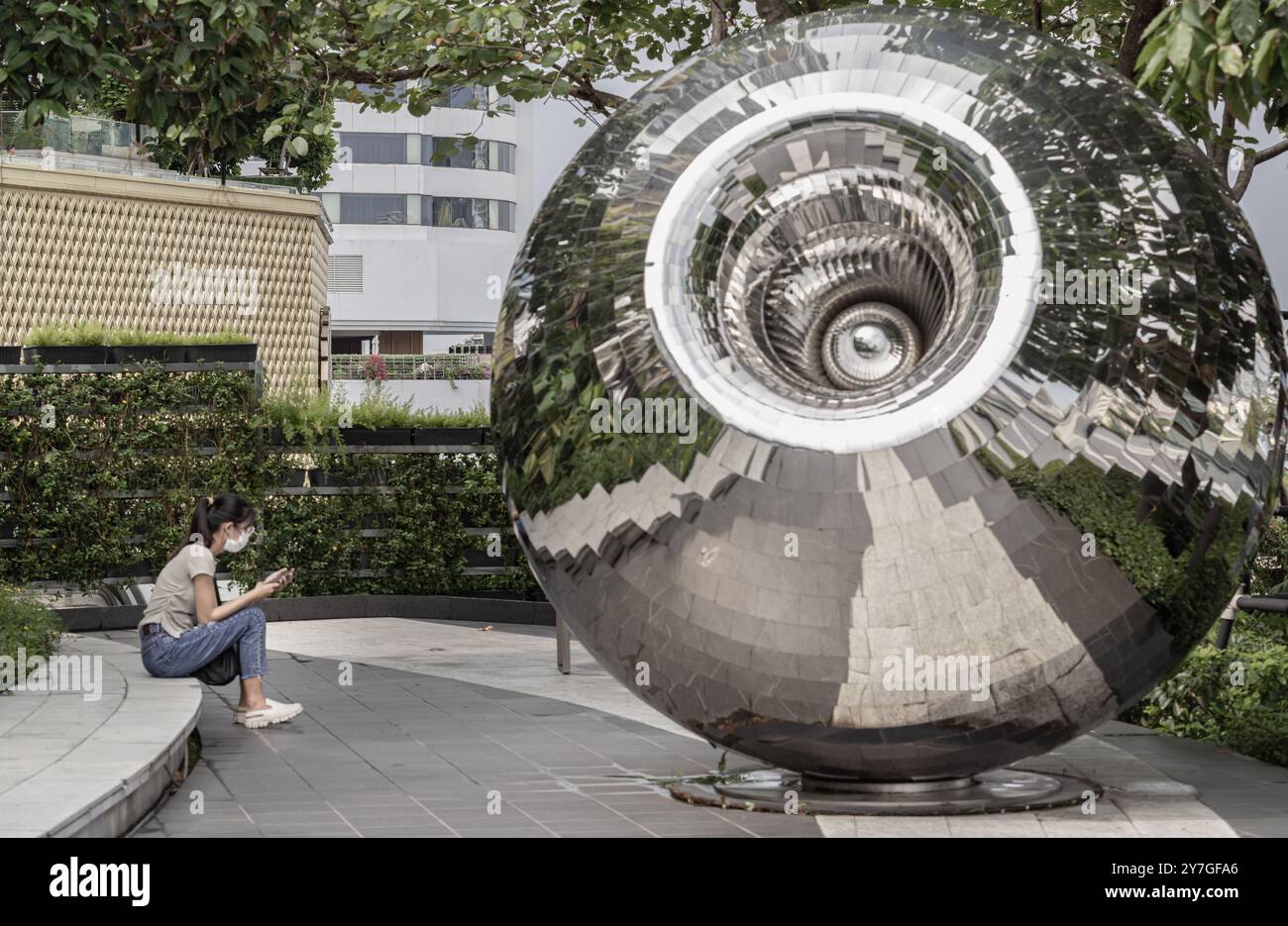 Bangkok,​ Thailand - 28. September 2024 - eine unbekannte junge Frau, die ein eifarbiges T-Shirt mit Jeans und Schutzmaske trägt und ein Smartphone benutzt Stockfoto