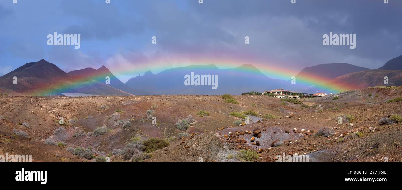 Regenbogenpanorama in vulkanischer Landschaft mit Bergen und zwei Häusern Stockfoto