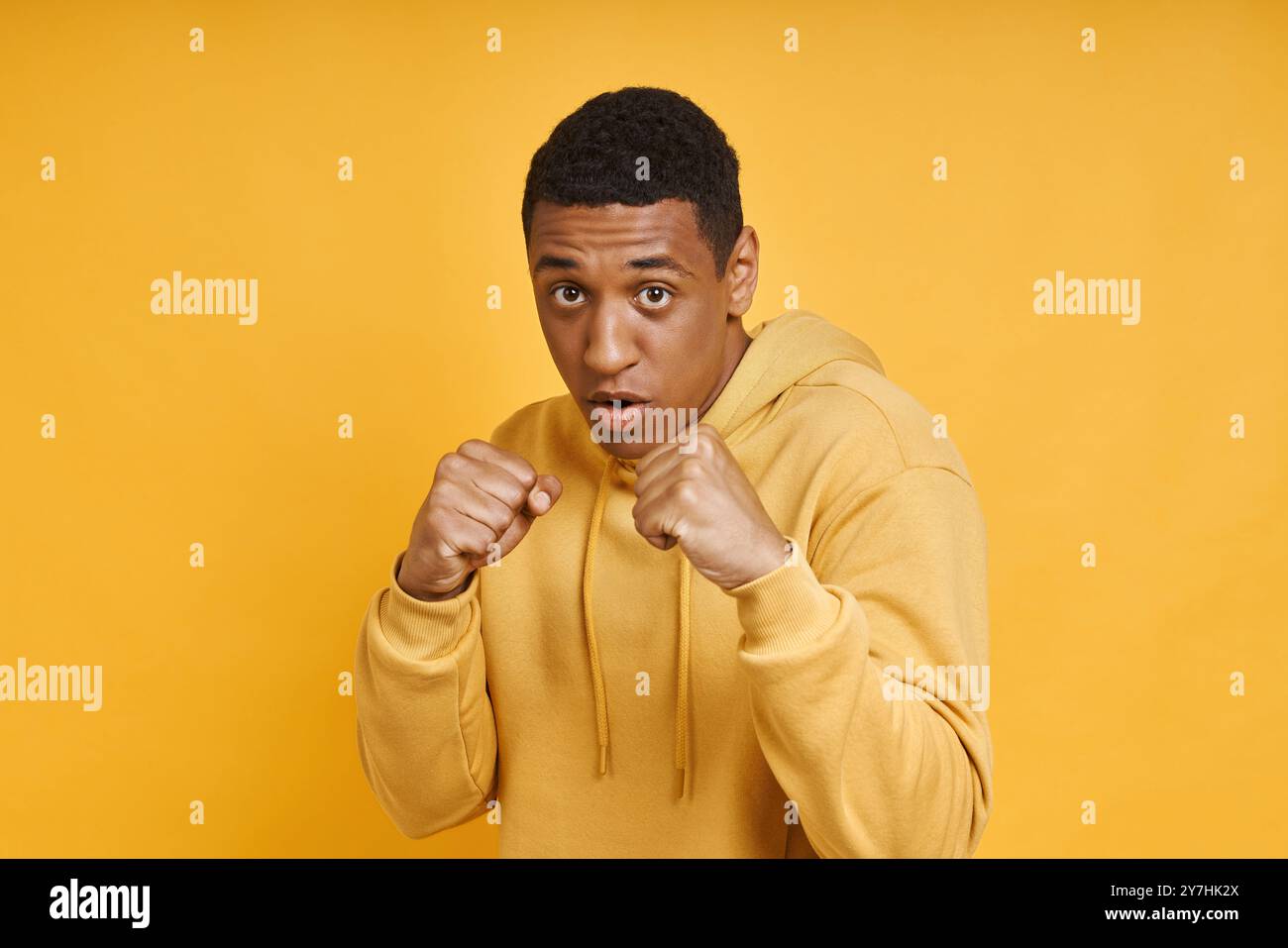 Selbstbewusster Mixed Race-Mann, der in Boxposition vor gelbem Hintergrund steht Stockfoto
