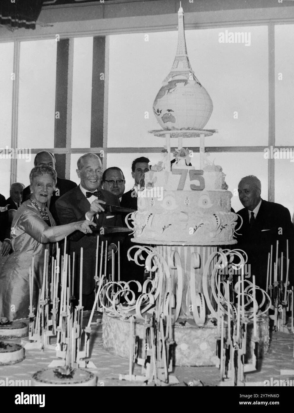 Am 16. MAI 1964 feierte der Eiffelturm. Die Schauspielerin Beatrix Dussane und die Sängerin Maurice Chevalier zerschnitten am 15. Mai die Tortenlawine, die am Eiffelturm stattfand, um den 75. Geburtstag des gefeierten Turms zu feiern. Die Gäste des Mittagessens beinhalteten Pariser VIPs, die 75 Jahre alt sind. Die Kuchenüberwindung ist ein Modell der Weltkugel, auf der sich ein Modell des berühmten Turms befindet. Paris, Frankreich Stockfoto