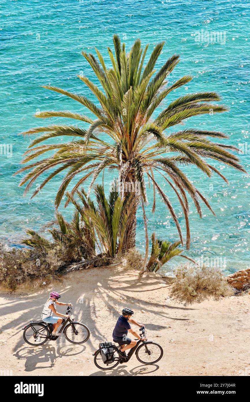 Unbekanntes älteres Ehepaar, das auf Fahrrädern entlang der Mittelmeerküste mit wunderschönem Blick auf die Natur und die Palmen fährt. Reise, touristischer Ort. Stockfoto