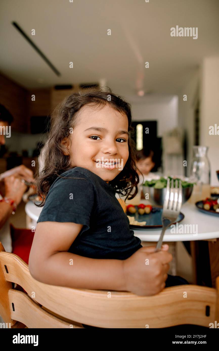 Seitliches Porträt eines lächelnden Jungen, der über die Schulter schaut, während er die Gabel zu Hause hält Stockfoto
