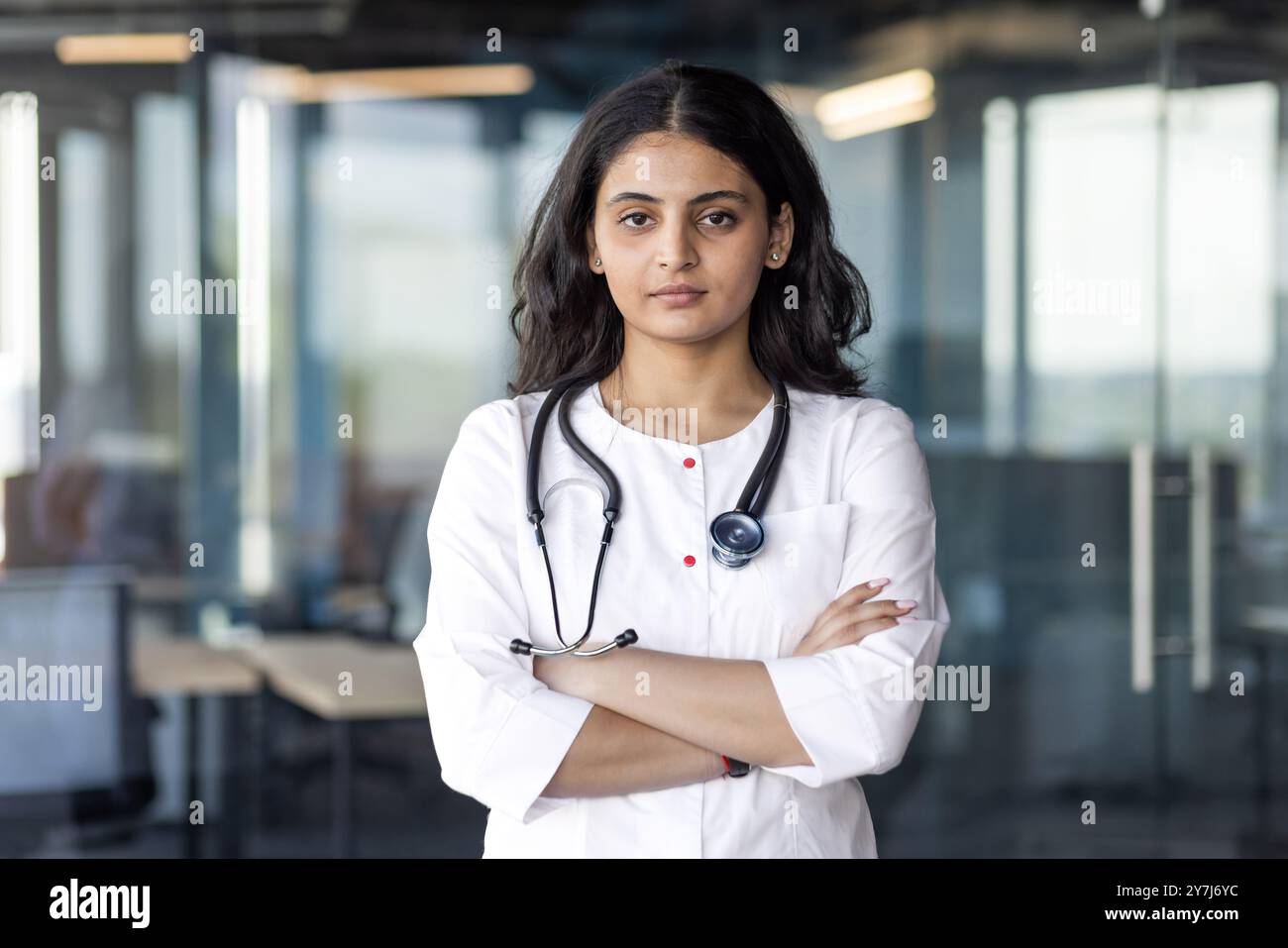 Selbstbewusste Ärztin mit Stethoskop um den Hals gekreuzte Arme in der modernen Praxis. Professioneller Ausdruck, medizinisches Umfeld. Steht für Gesundheitswesen, Vertrauen und Engagement. Stockfoto