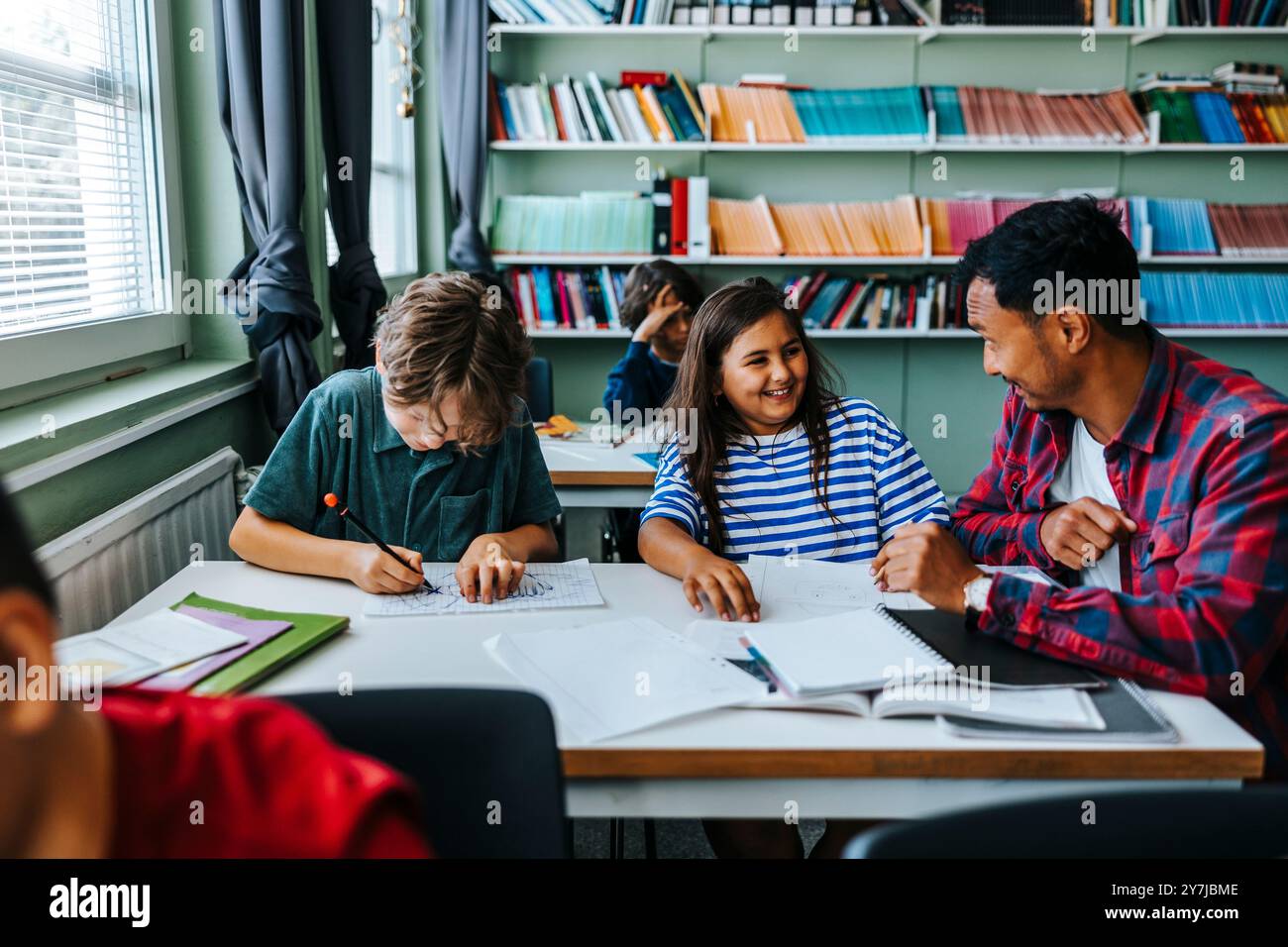 Männlicher Lehrer, der in der Nähe von weiblichen und männlichen Grundschülern sitzt Stockfoto