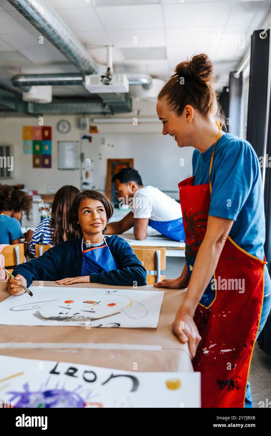 Lächelnde Kunstprofessorin, die männlichen Schüler während des Kunstunterrichts in der Schule unterstützt Stockfoto
