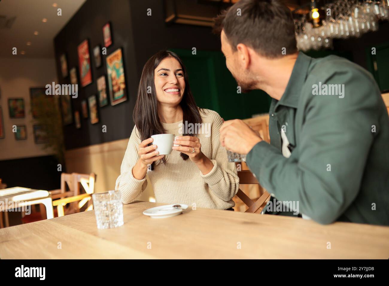Zwei Freunde teilen sich Lachen und warme Drinks in einem charmanten Café und schaffen eine einladende Atmosphäre, die an einem sonnigen Tag die Verbindung und Freude feiert Stockfoto