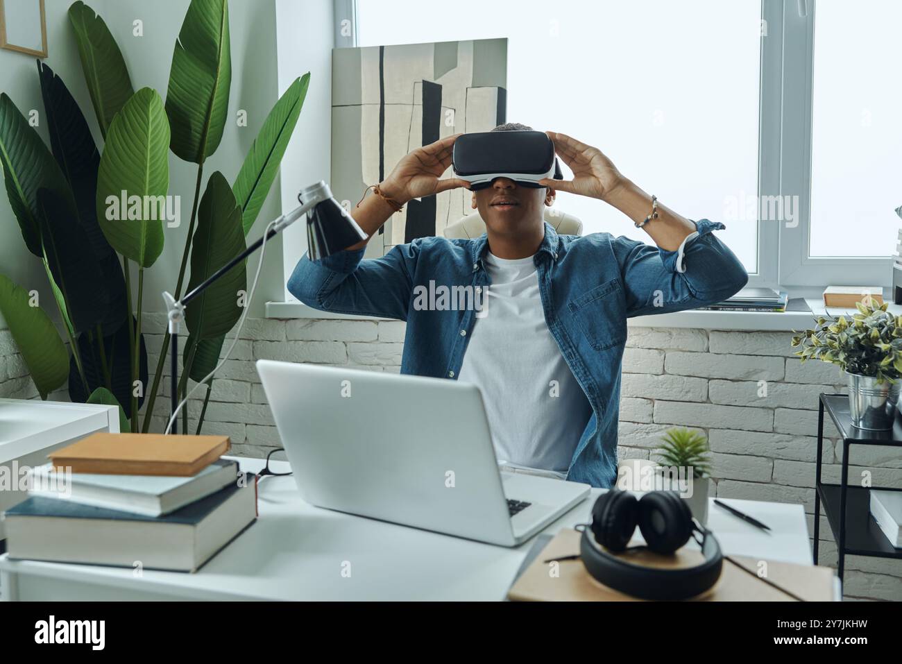 Junger Mann mit einer Virtual-Reality-Brille, während er am Arbeitsplatz sitzt Stockfoto