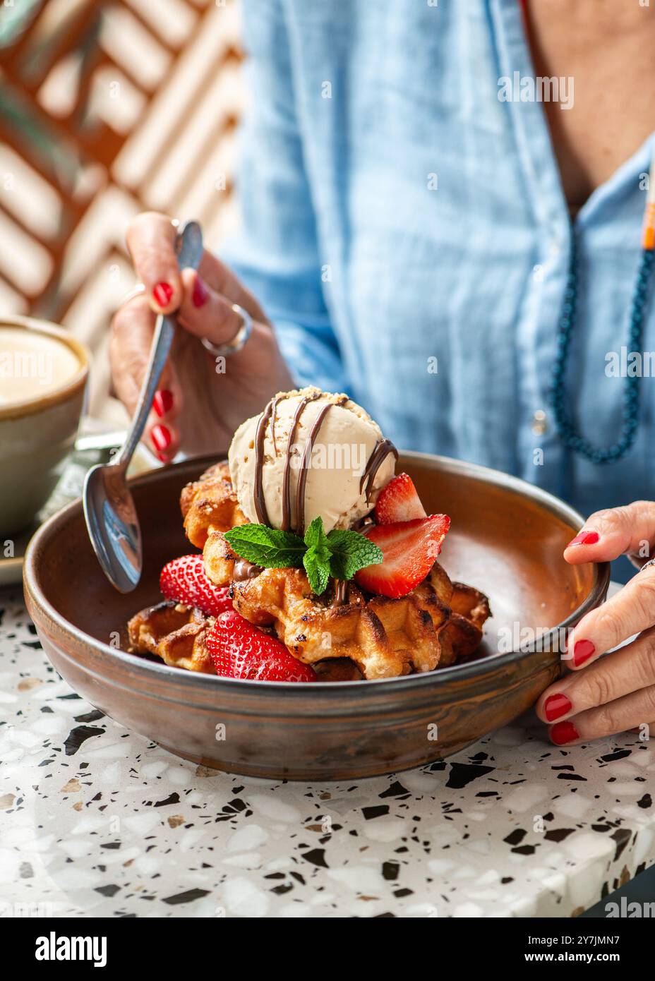 Eine Frau isst amerikanische Waffeln mit Eis, Erdbeeren, Ahornsirup und dunklen Schokoladenchips. Stockfoto