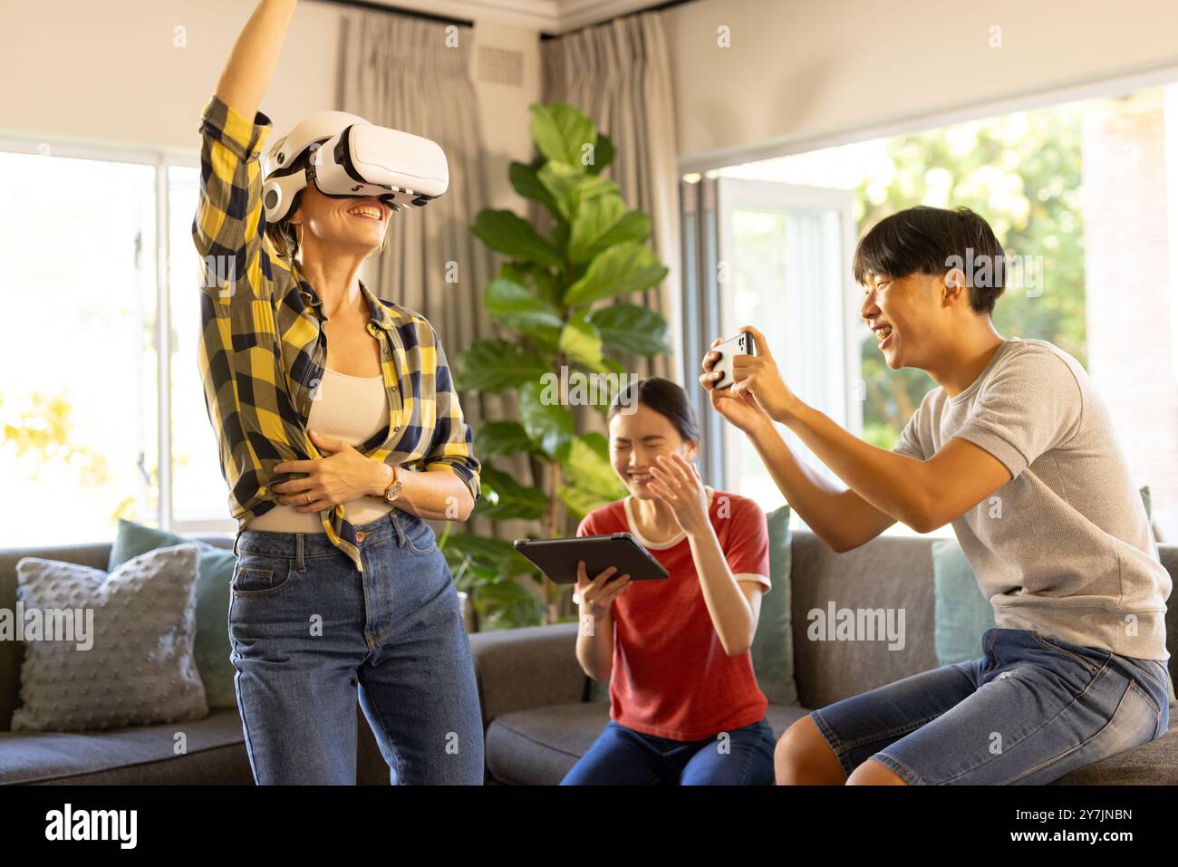 Beim Spielen des VR-Spiels trägt die Mutter ein VR-Headset, während die Familie anfeuert und das Tablet verwendet Stockfoto