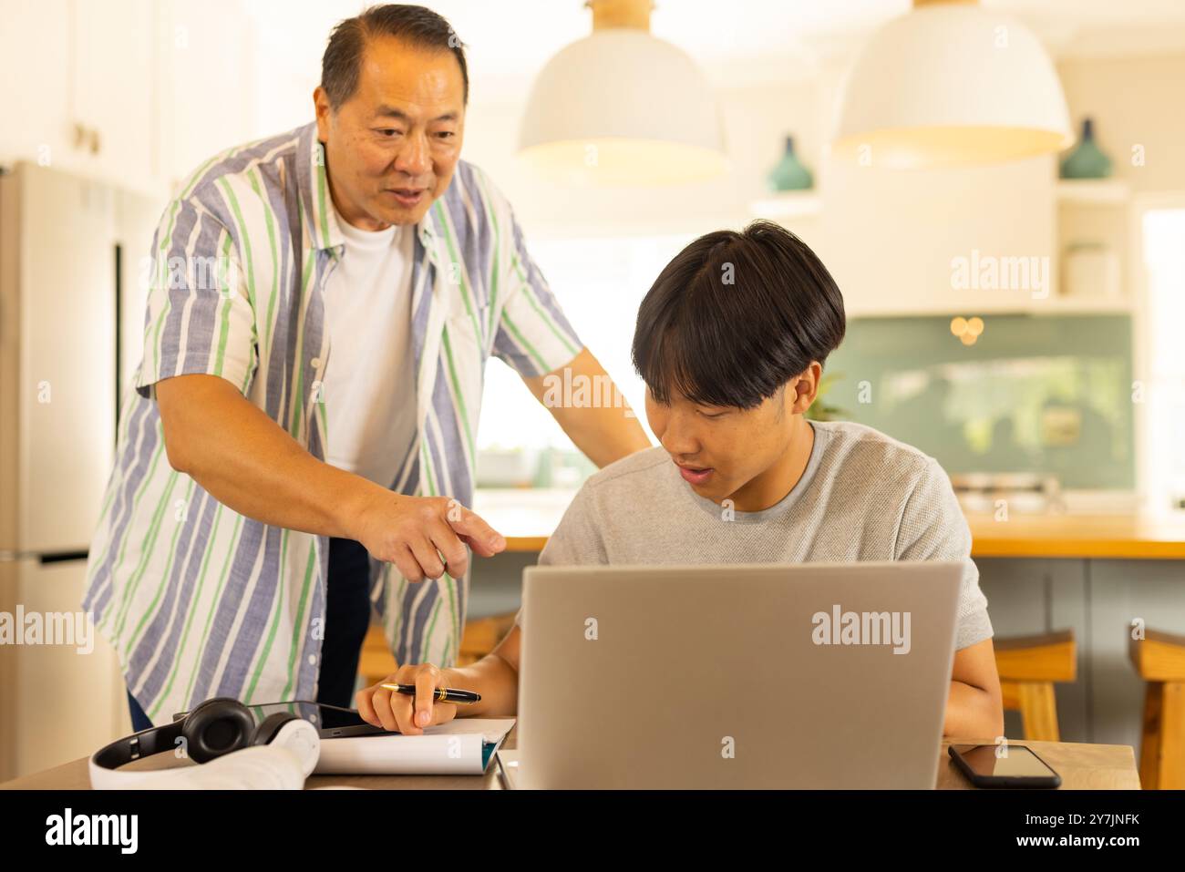 Asiatischer Vater zeigt auf Laptop, während Sohn zu Hause an Schulprojekten arbeitet Stockfoto