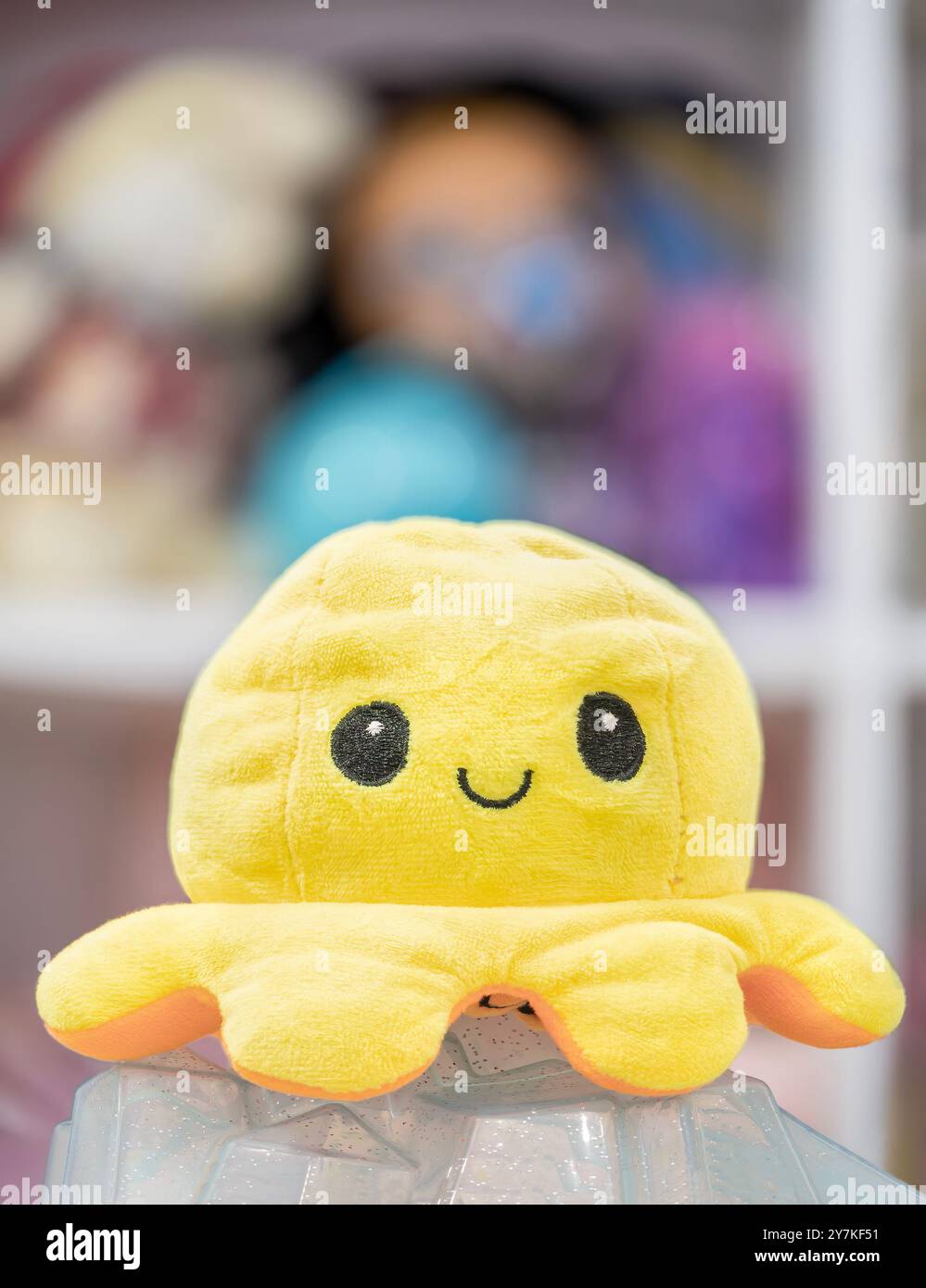 Gelber Plüschkrake im Vordergrund steht ein gelbes Plüschtier in der Form eines Tintenfischs. Sein lächelndes Gesicht verleiht einen Hauch von Laune. Stockfoto