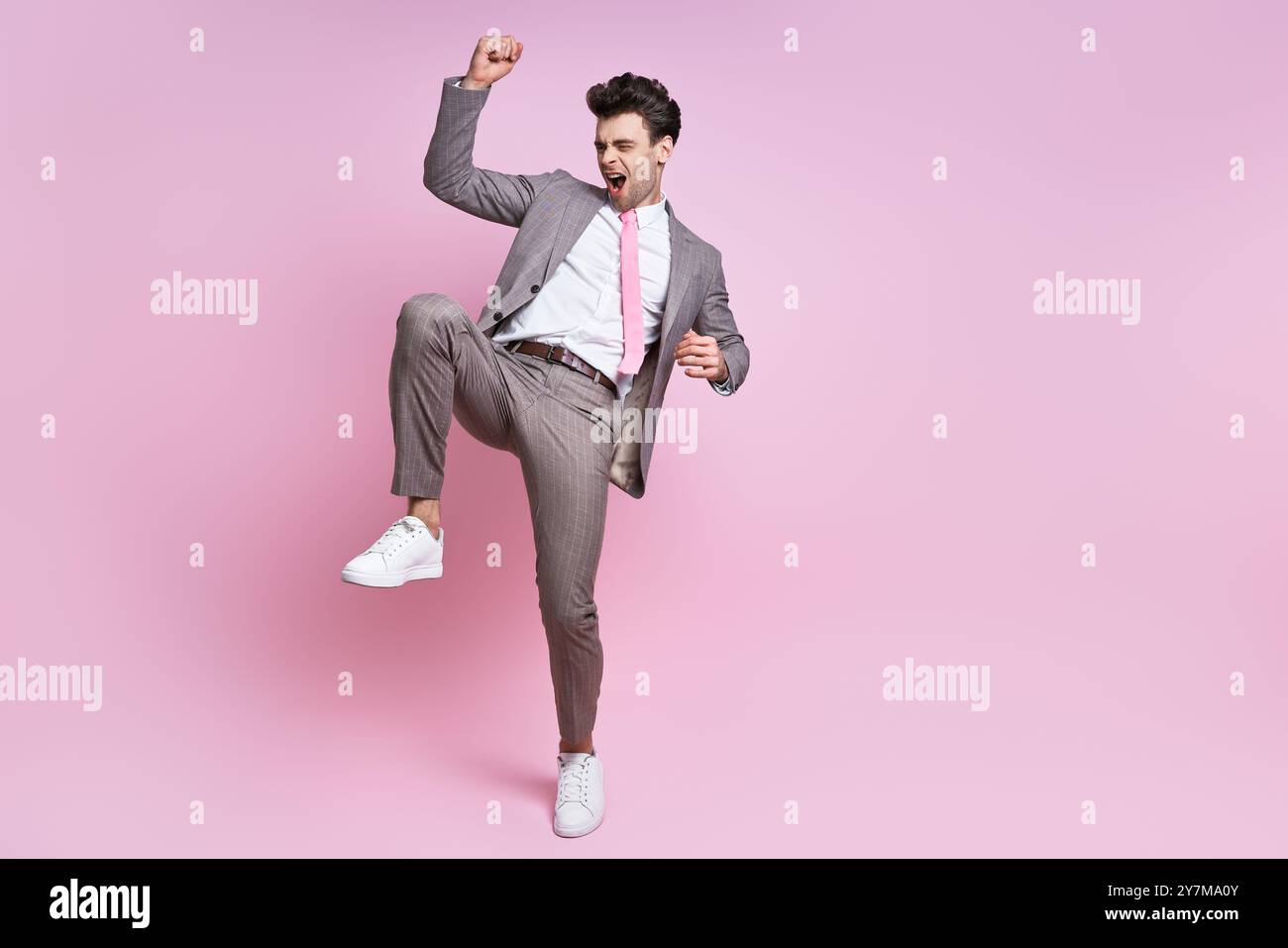 Aufgeregter junger Mann im Vollanzug, der vor rosa Hintergrund steht Stockfoto