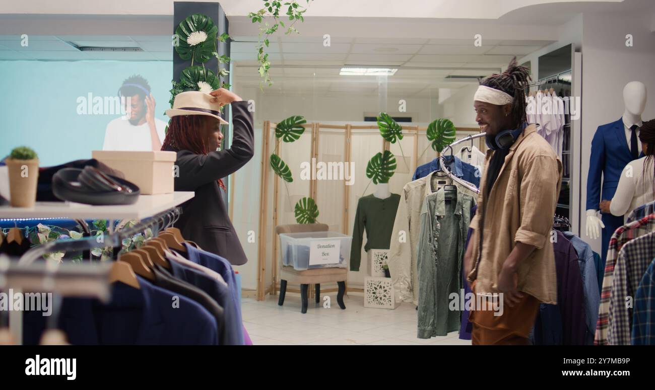 Beste Freunde, die professionelle Tanzbewegungen in Second-Shop mit Vintage-Kleidung machen. Mann und Frau, die Spaß beim Tanzen in einem erstklassigen Second-Hand-Bekleidungsgeschäft haben, das alte Kleidung verkauft Stockfoto
