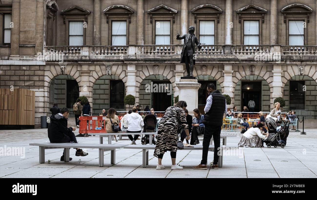 London, England, April 30 2023: Menschen sitzen draußen bei einer Bronzestatue an einem hellen Tag Stockfoto