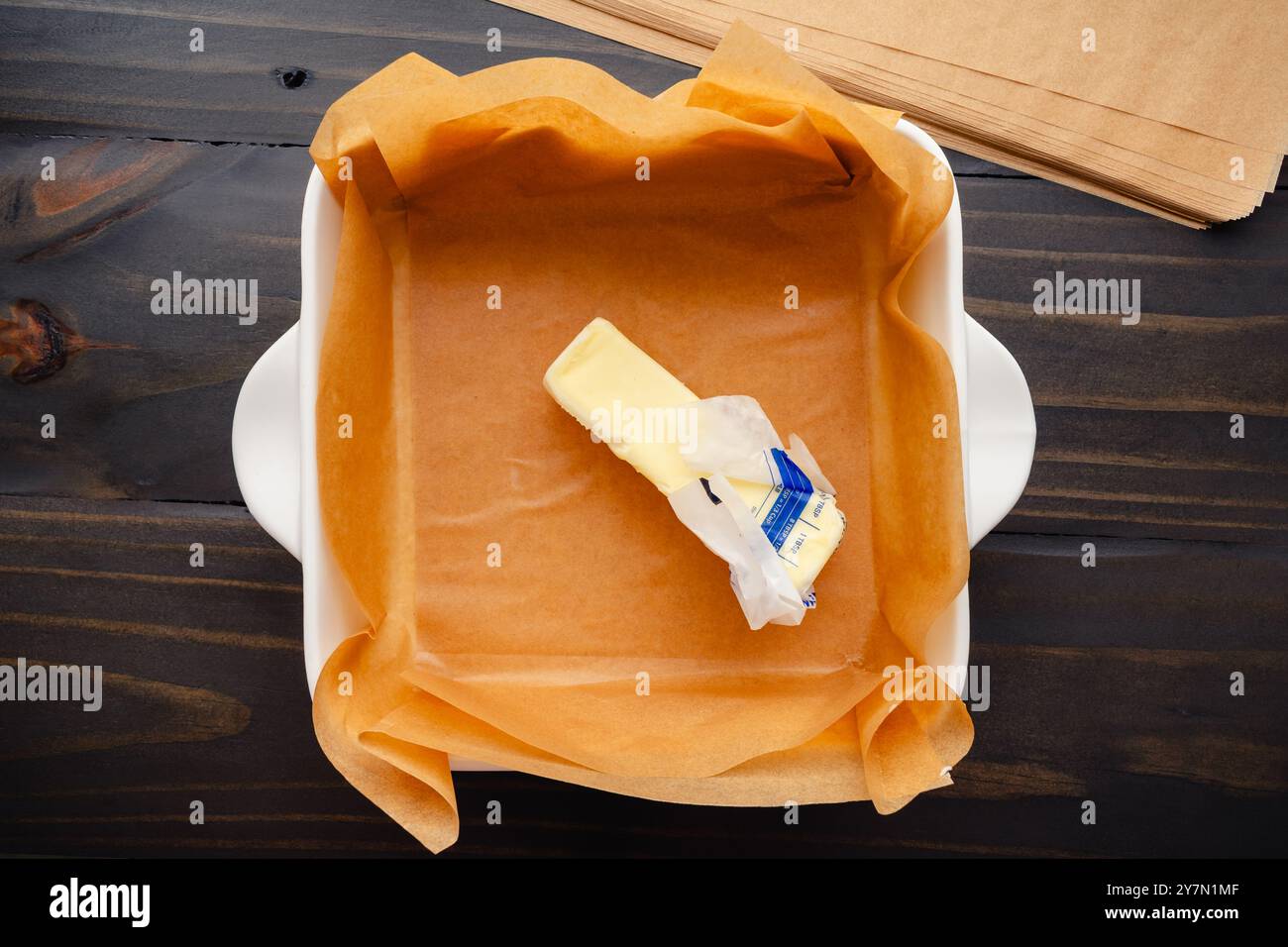 Butterstab in einer quadratischen Backform mit Pergament: Ungebleichtes Backpapier, gefettet mit einem Butterstab in einer Keramikform Stockfoto
